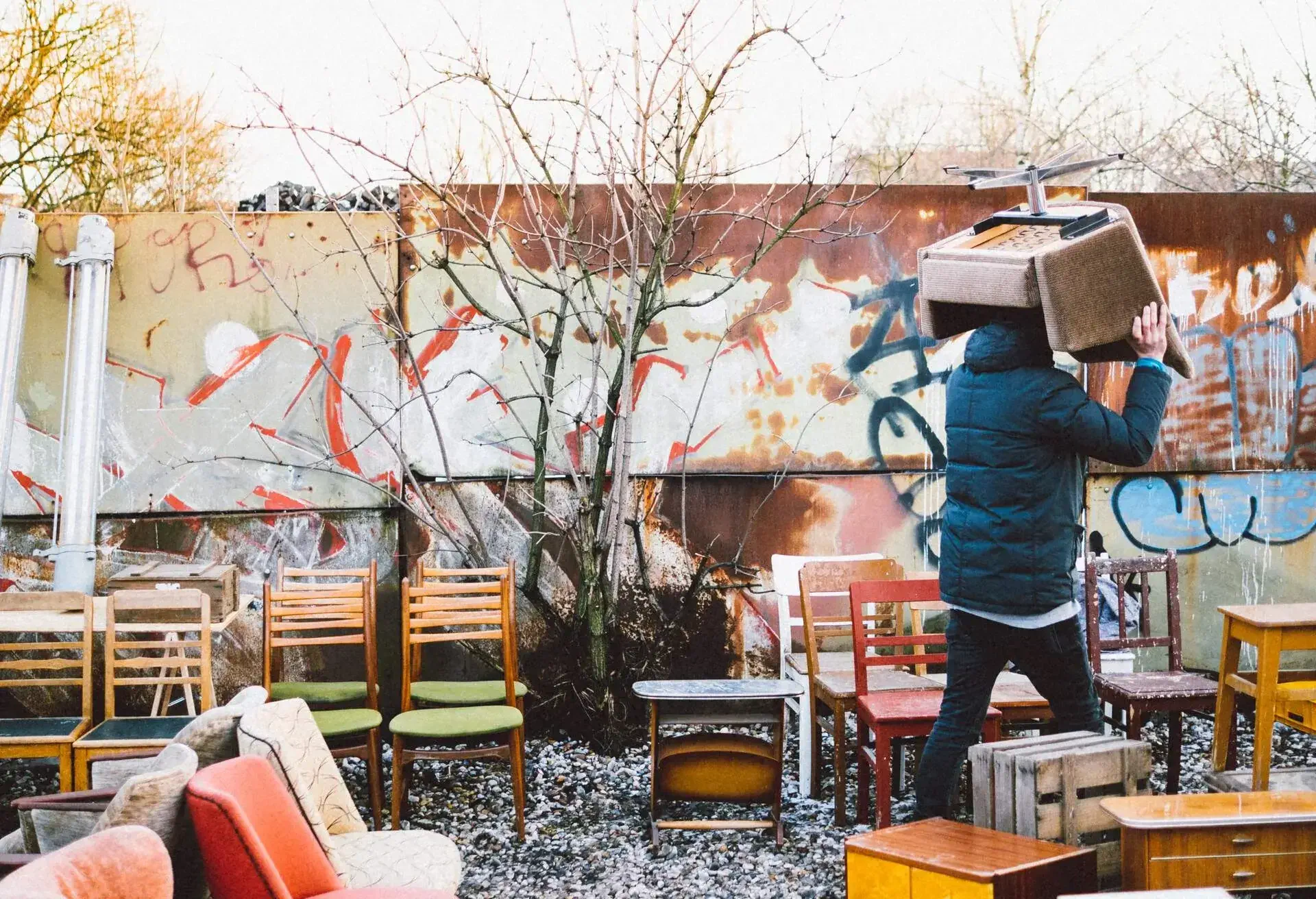 A man at an outdoor furniture store carrying a chair over his head.