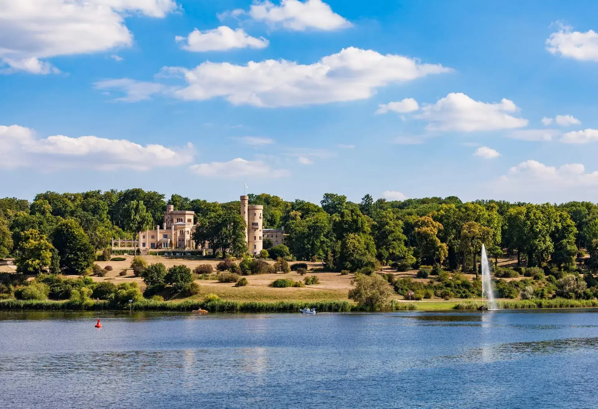 A lakeside castle with a large garden surrounded by thick and tall trees.