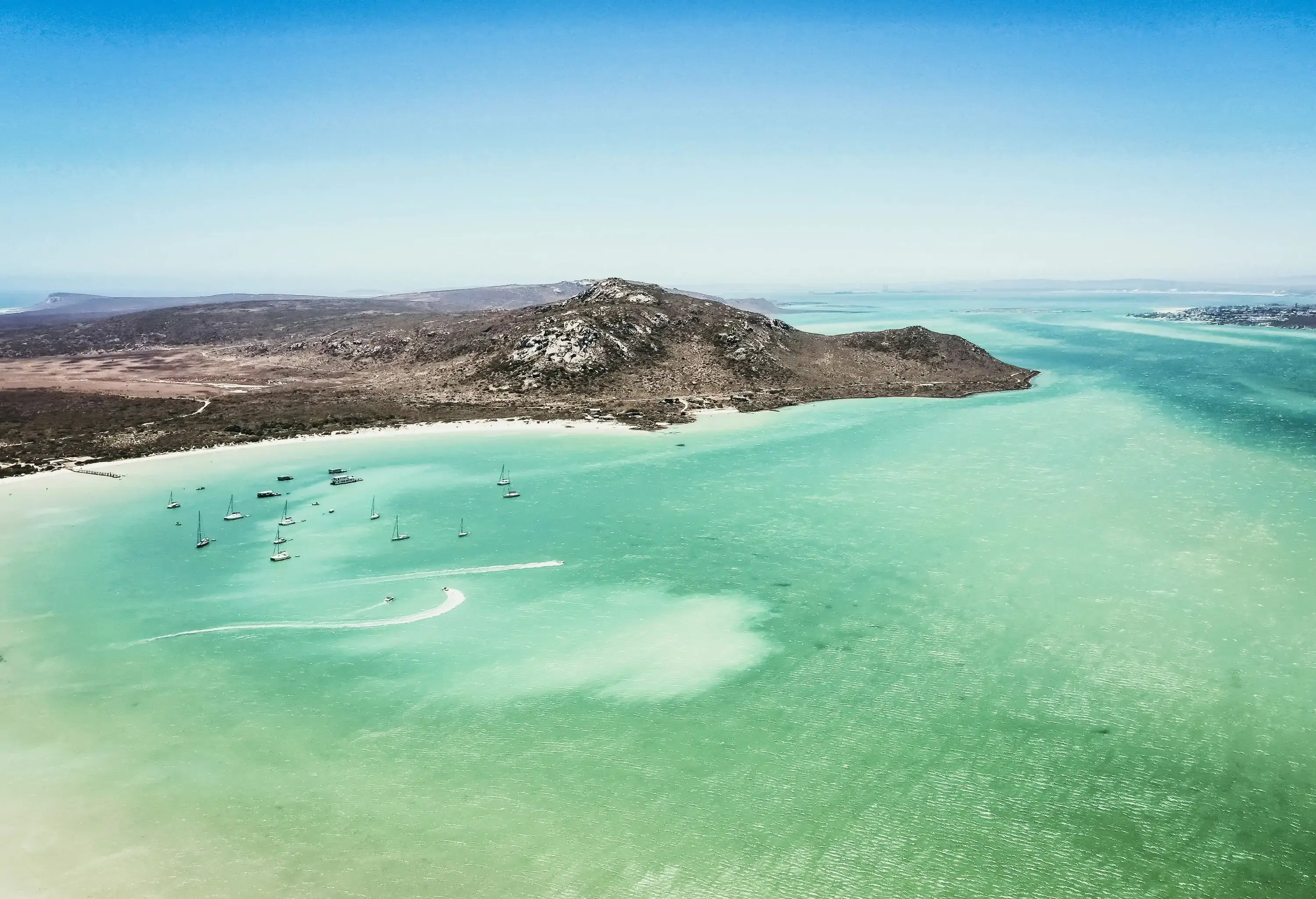 High angle view of a turquoise lagoon, boats in a bay with mountain in the background