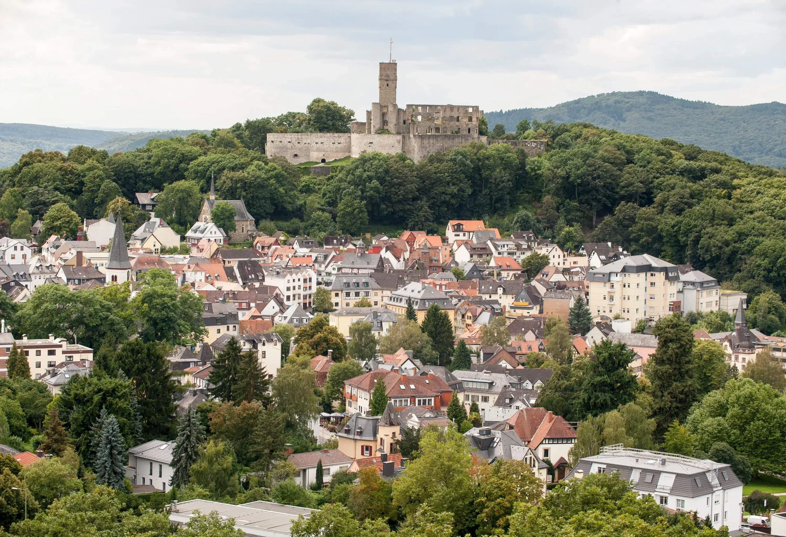 Towering castle ruins over a countryside village surrounded by greenery
