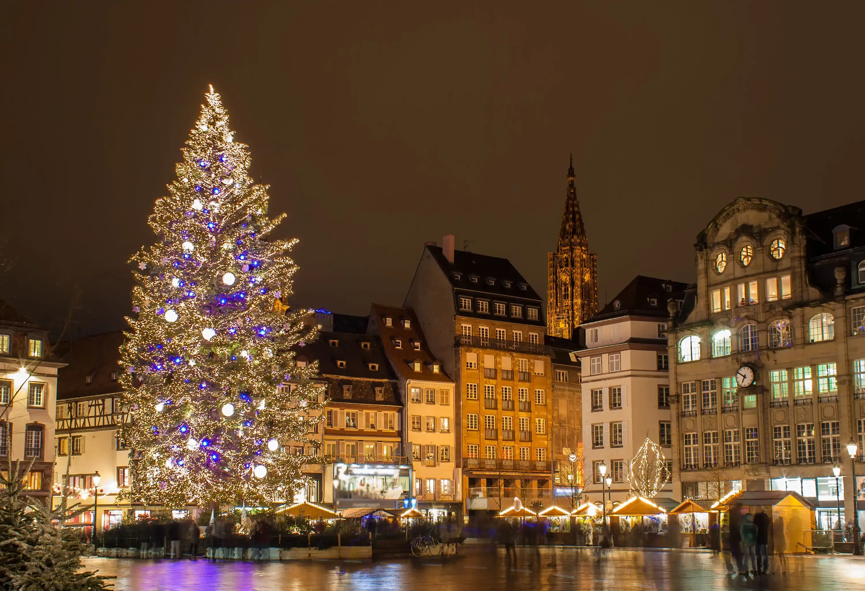 A beautiful Christmas tree filled with lights standing tall over the stores at a holiday market.