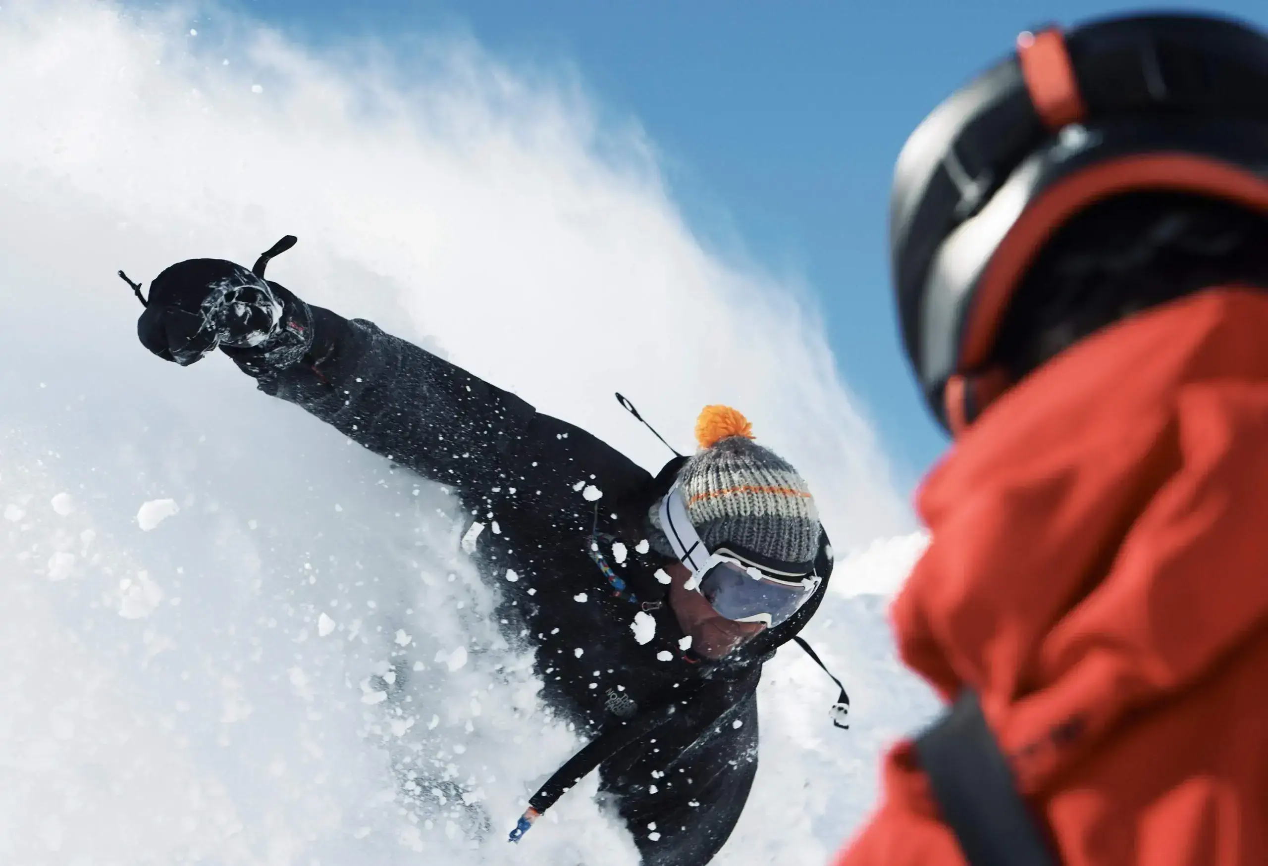 Two male skiers deep in powder snow splash.