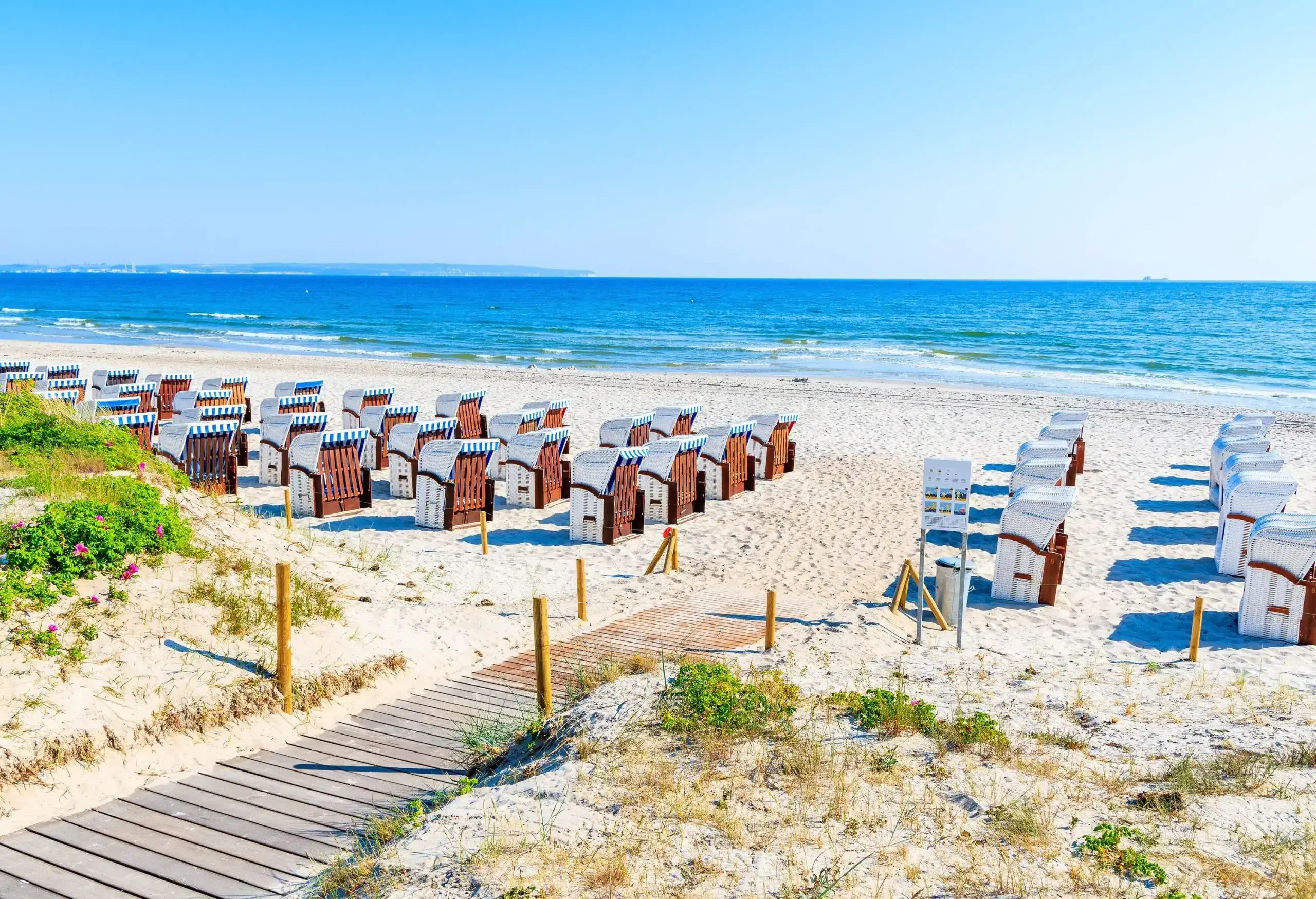 A white sand beach with a boardwalk and rows of canopied beach chairs.
