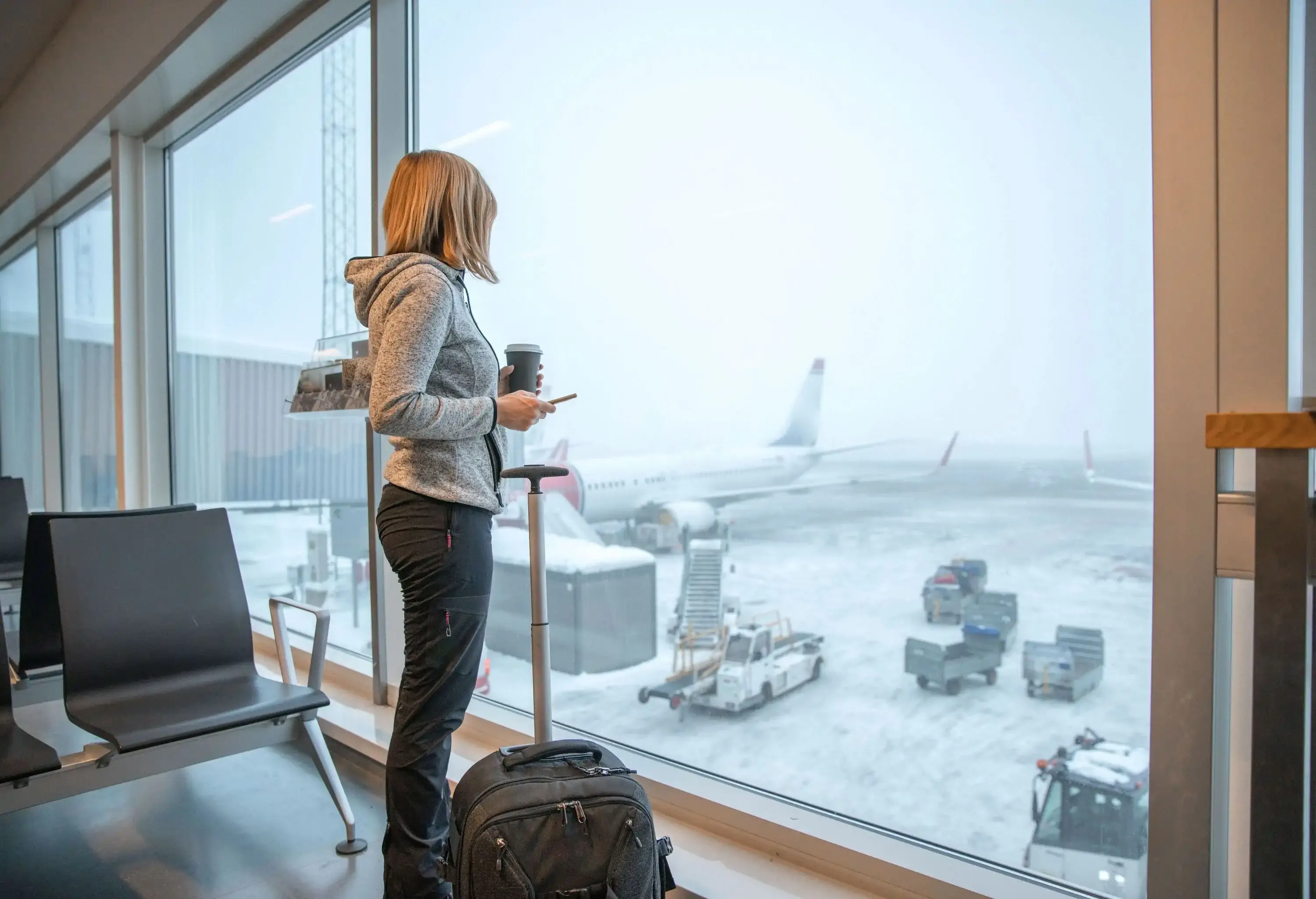 A woman with a carry-on bag looking through the window at the airport