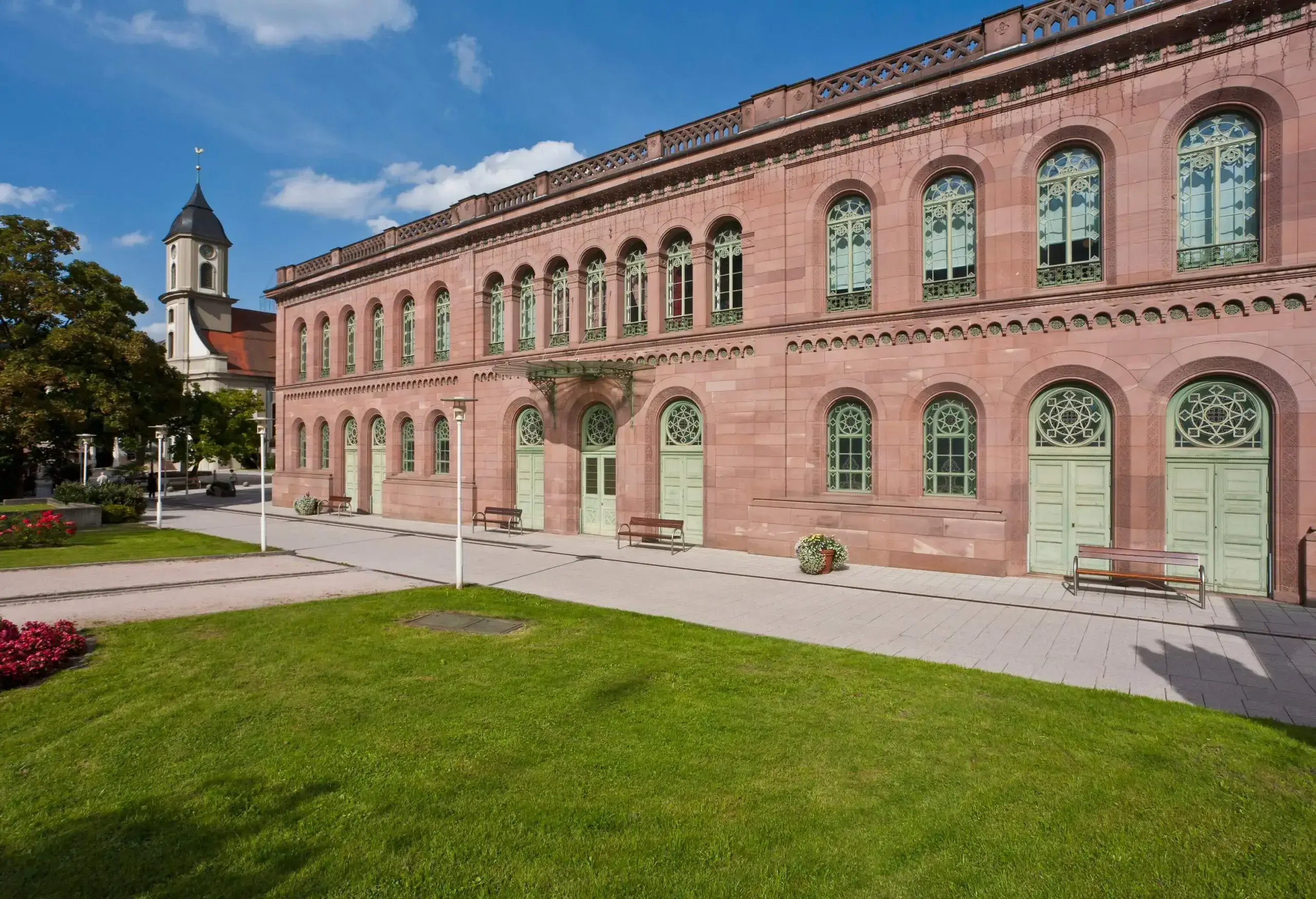 A broad, two-storey structure with several arch entrances and windows and a verdant lawn in front.