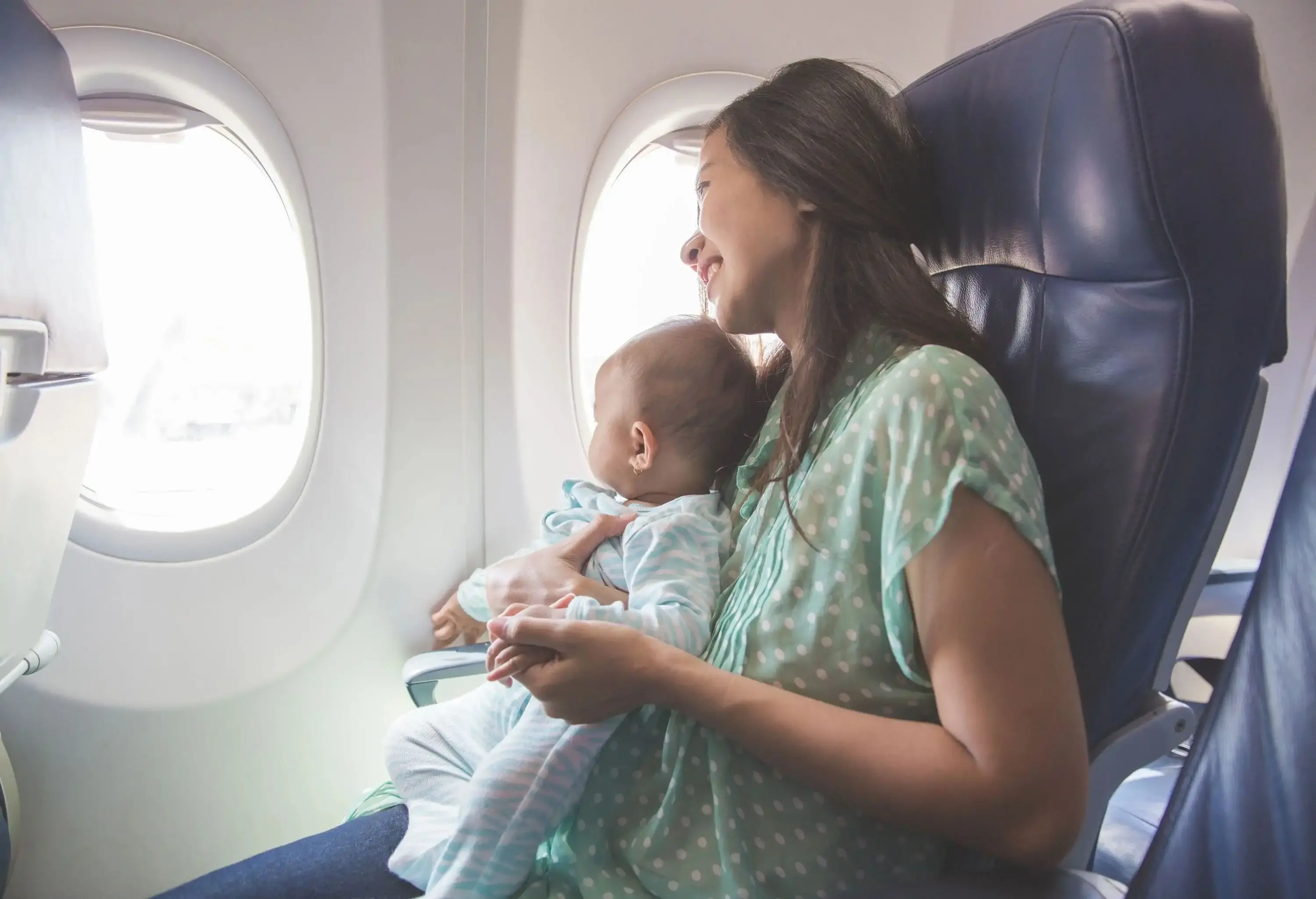 Baby sitting on mother's lap on a plane and looking through the window