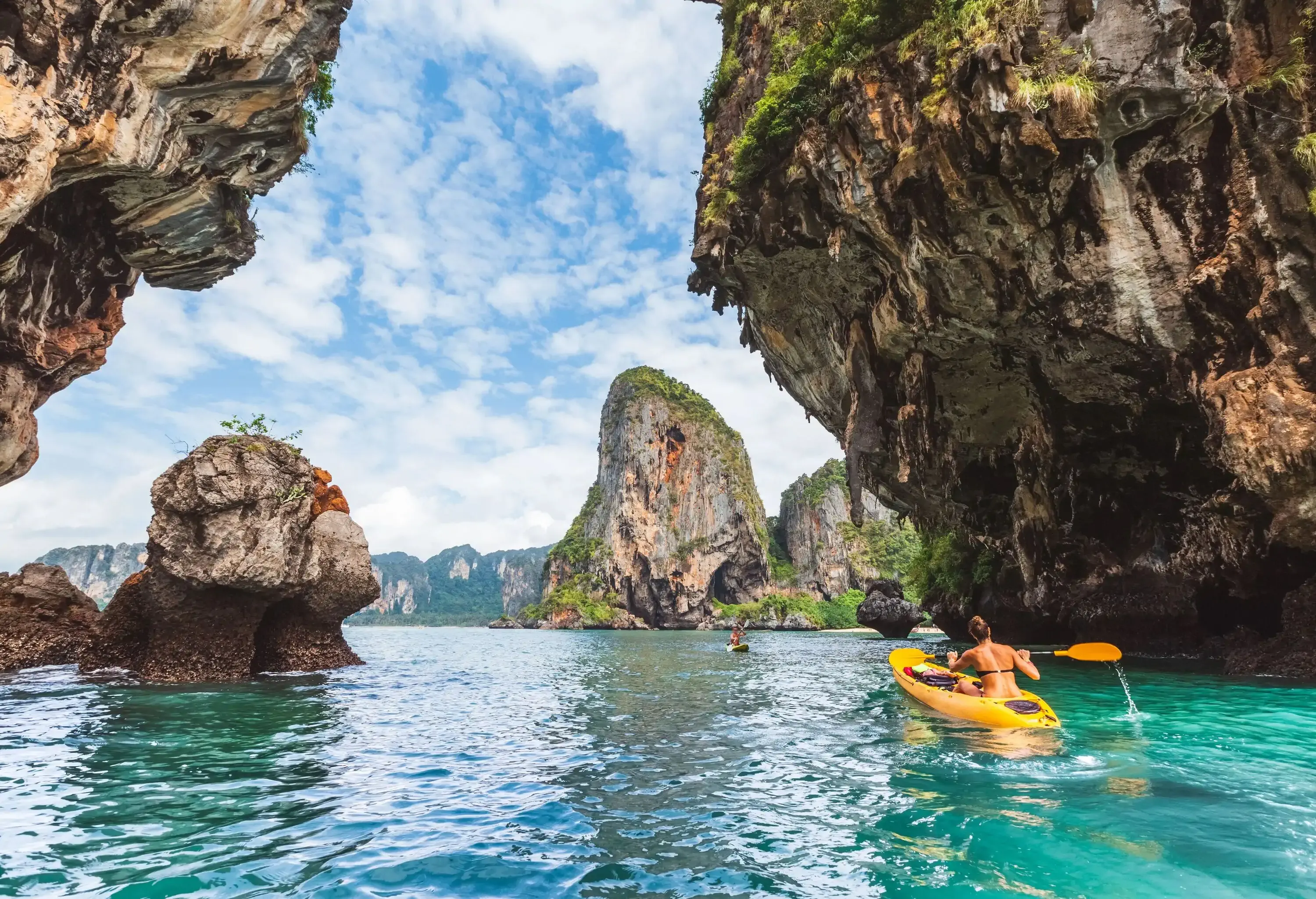 A woman rides a yellow kayak as she paddles along the steep rock cliffs of a beach.