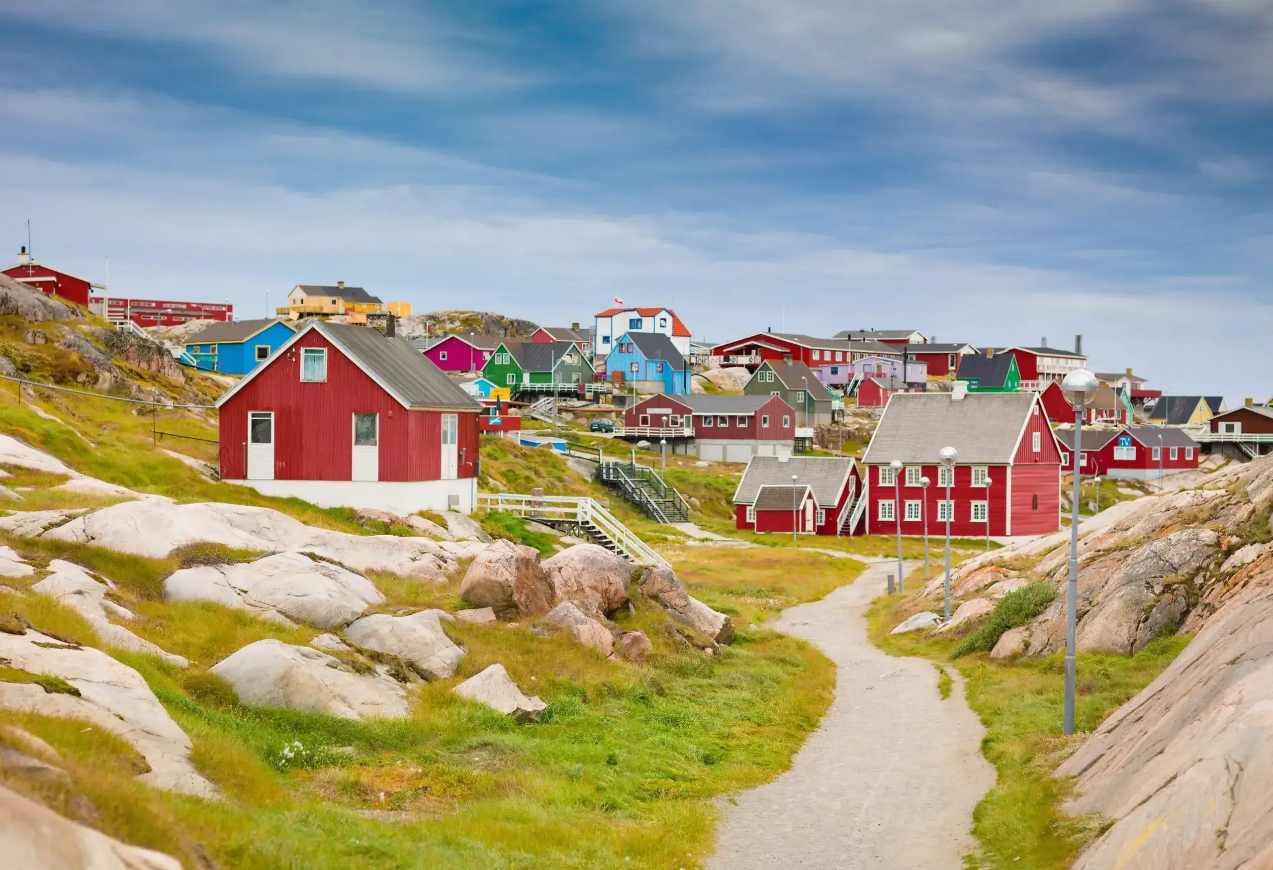 Wooden houses in vibrant multi-colours spread throughout the small hills against the dramatic sky.