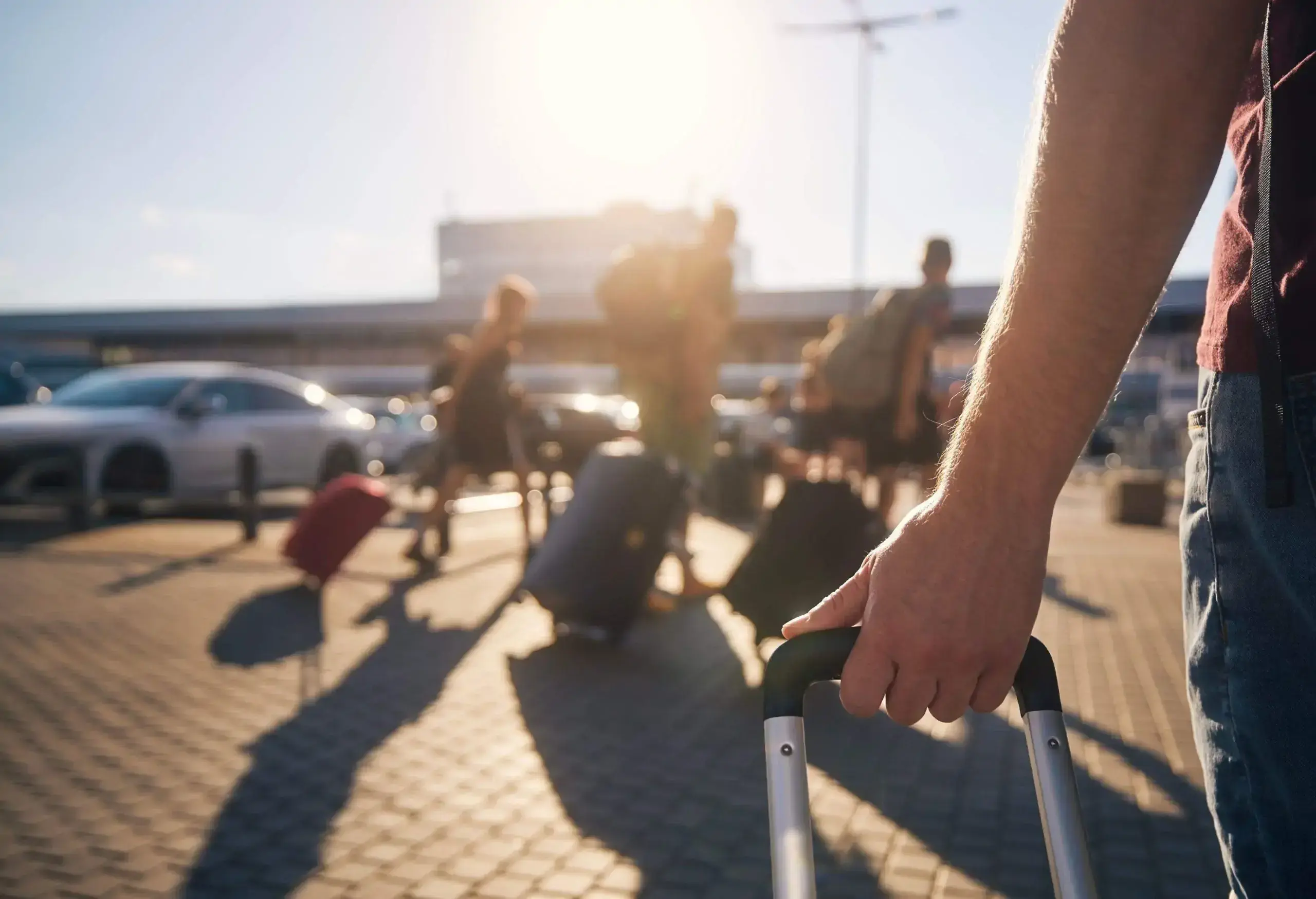 Group of people walking to airport terminal at summer sunset. Selective focus on hand of man with suitcase.