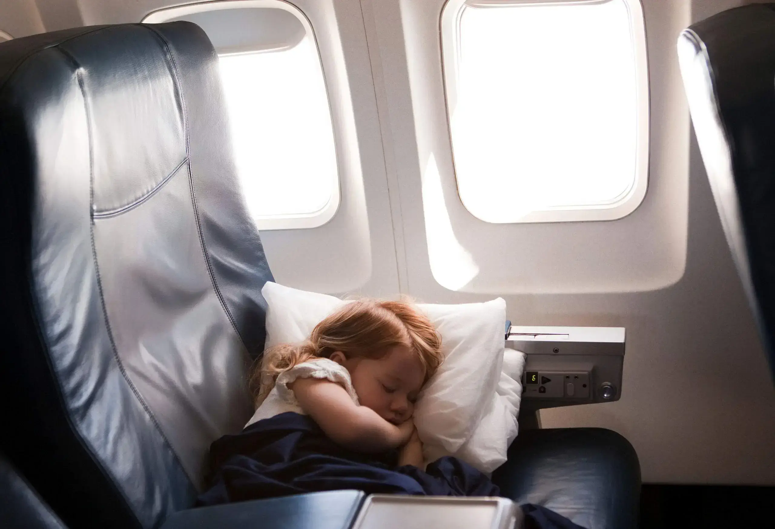 A little girl side-lying sleeps soundly on the airplane seat.