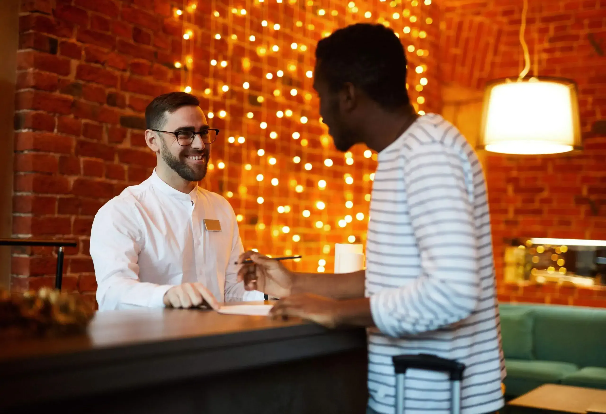 Happy hotel receptionist talking to foreign traveler by counter and helping him to register
