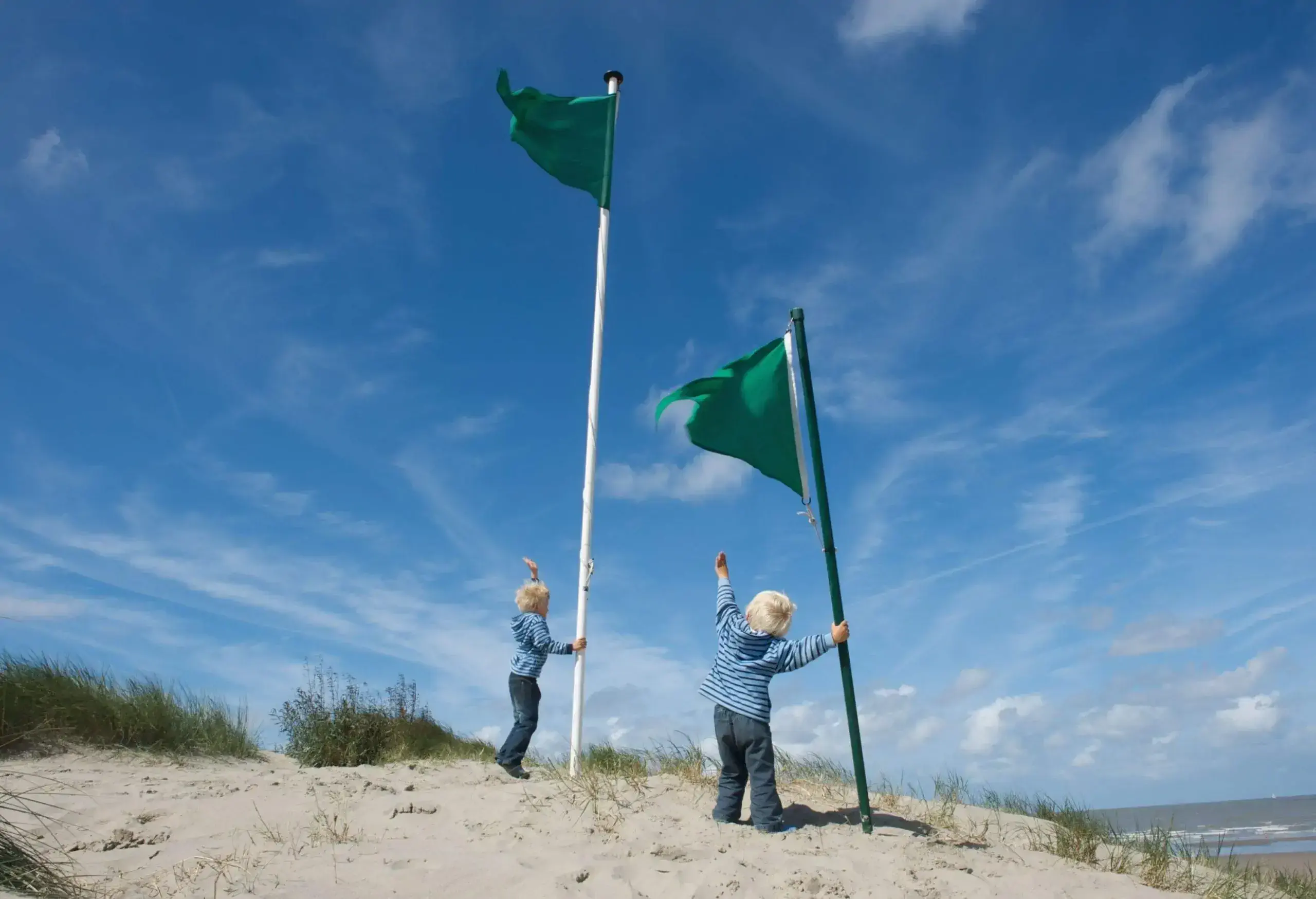 Two kids at a beach holding and looking up at two green flags