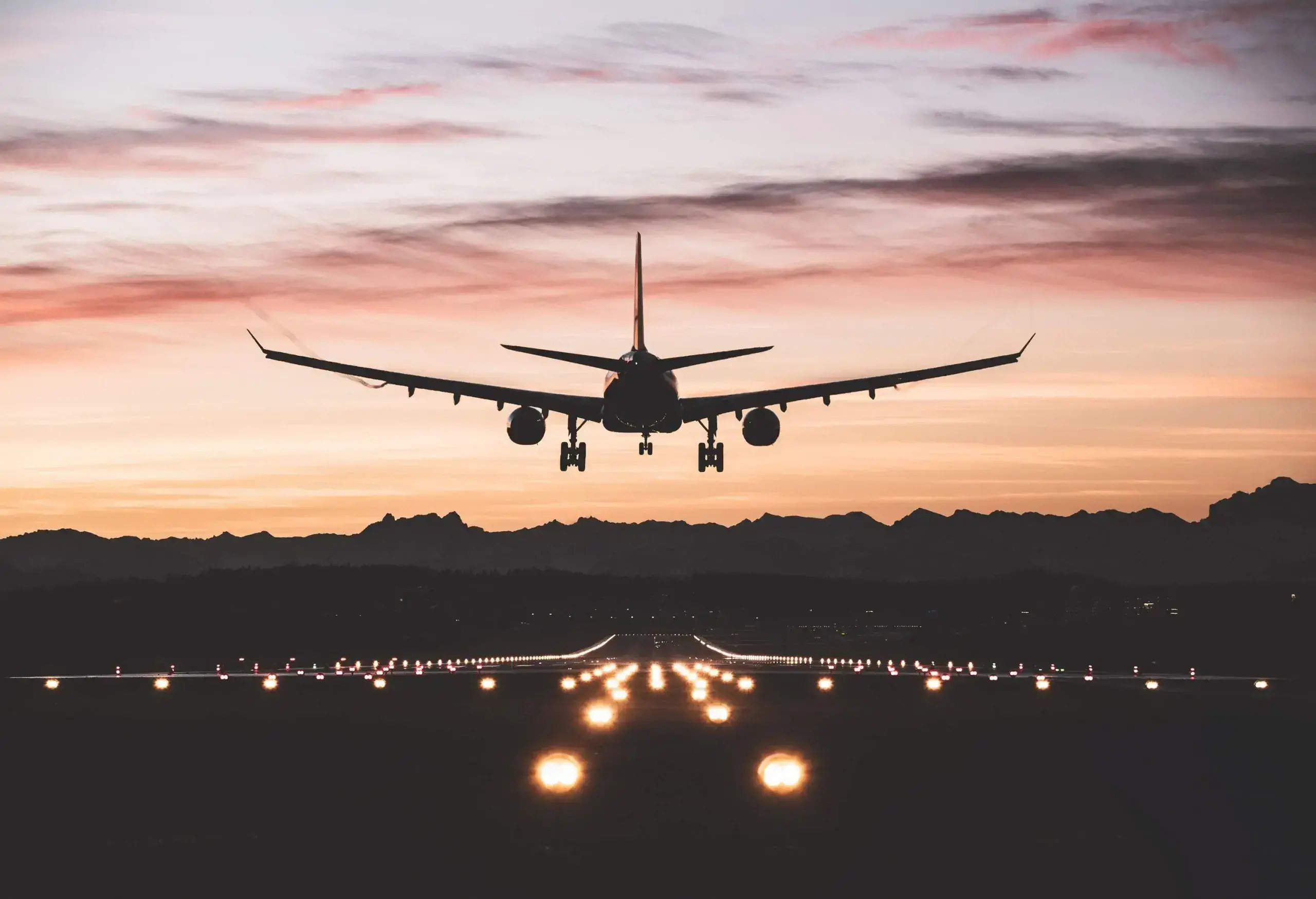 An airplane descending into a runway outlined by edge lights.