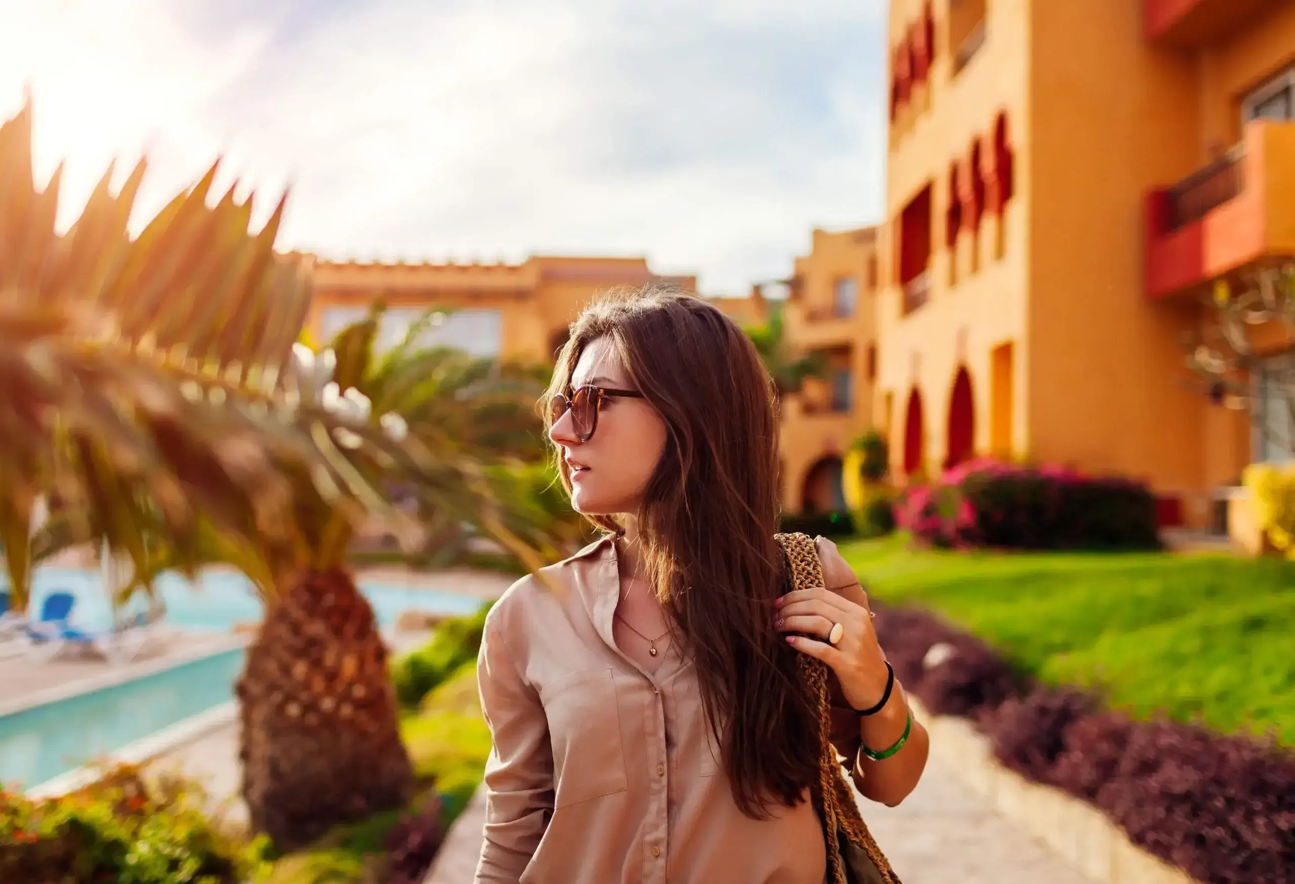 Portrait of young stylish woman walking by tropical palms in hotel yard in Egypt. Summer vacation on exotic resort