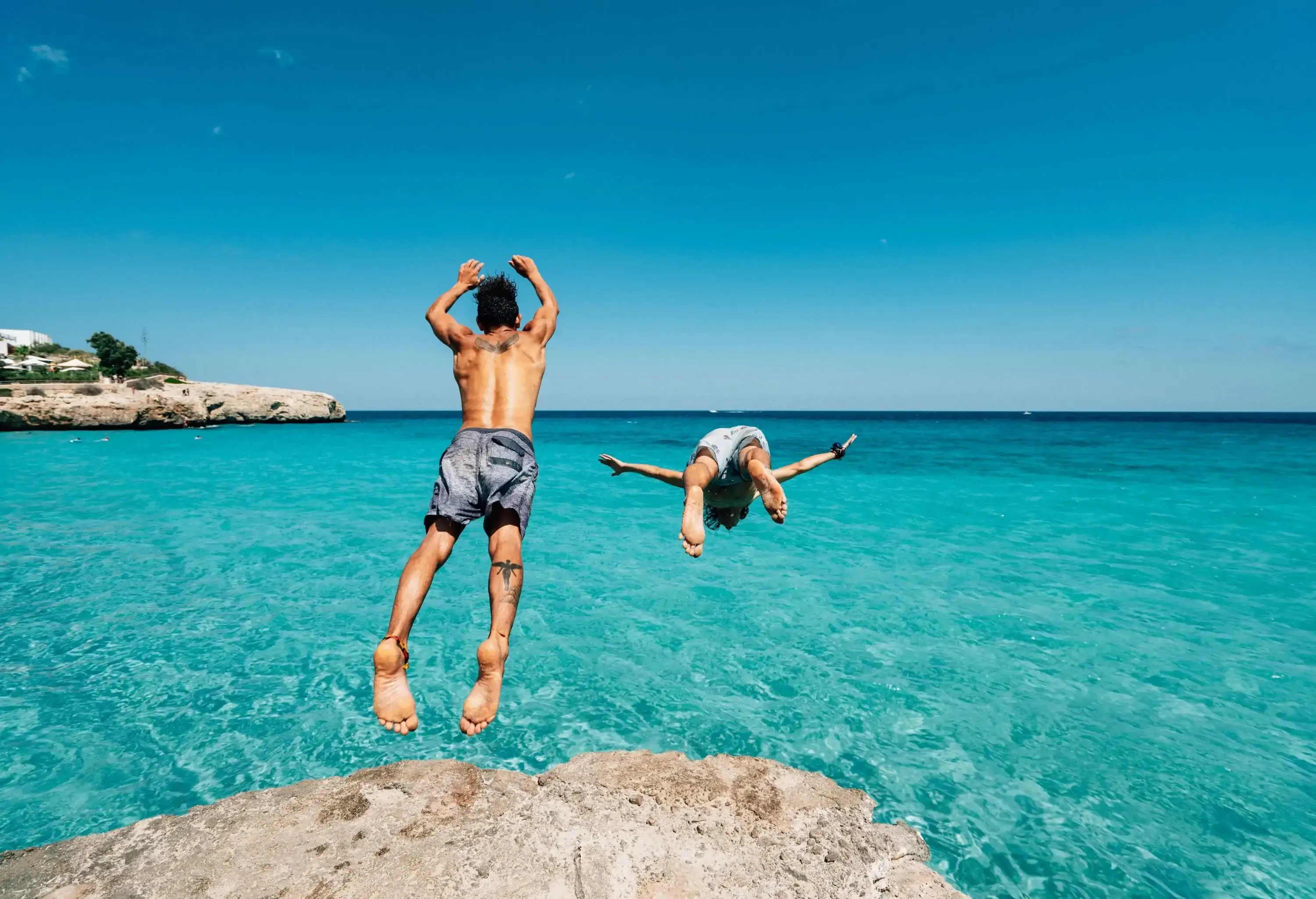 Two friends are diving in the sea from a cliff. Carefree, freedom, vacation concept.