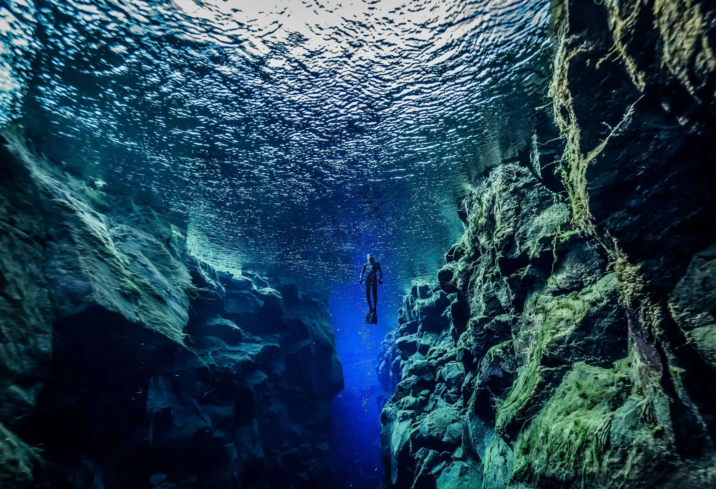 Underwater shot of diver in turquoise and blue water surrounded by rock formations