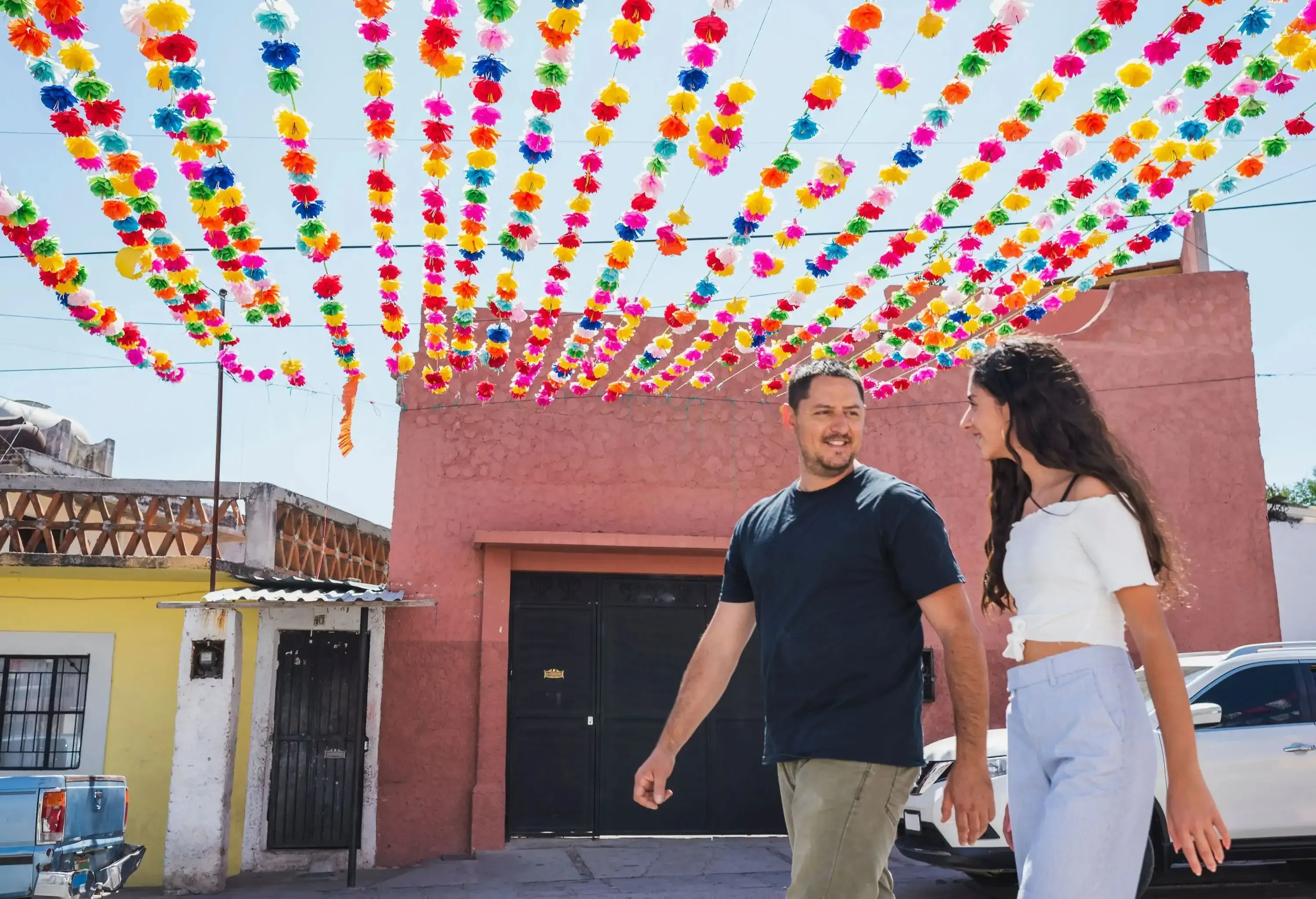 A man and a woman walking down the street under colourful paper flowers.