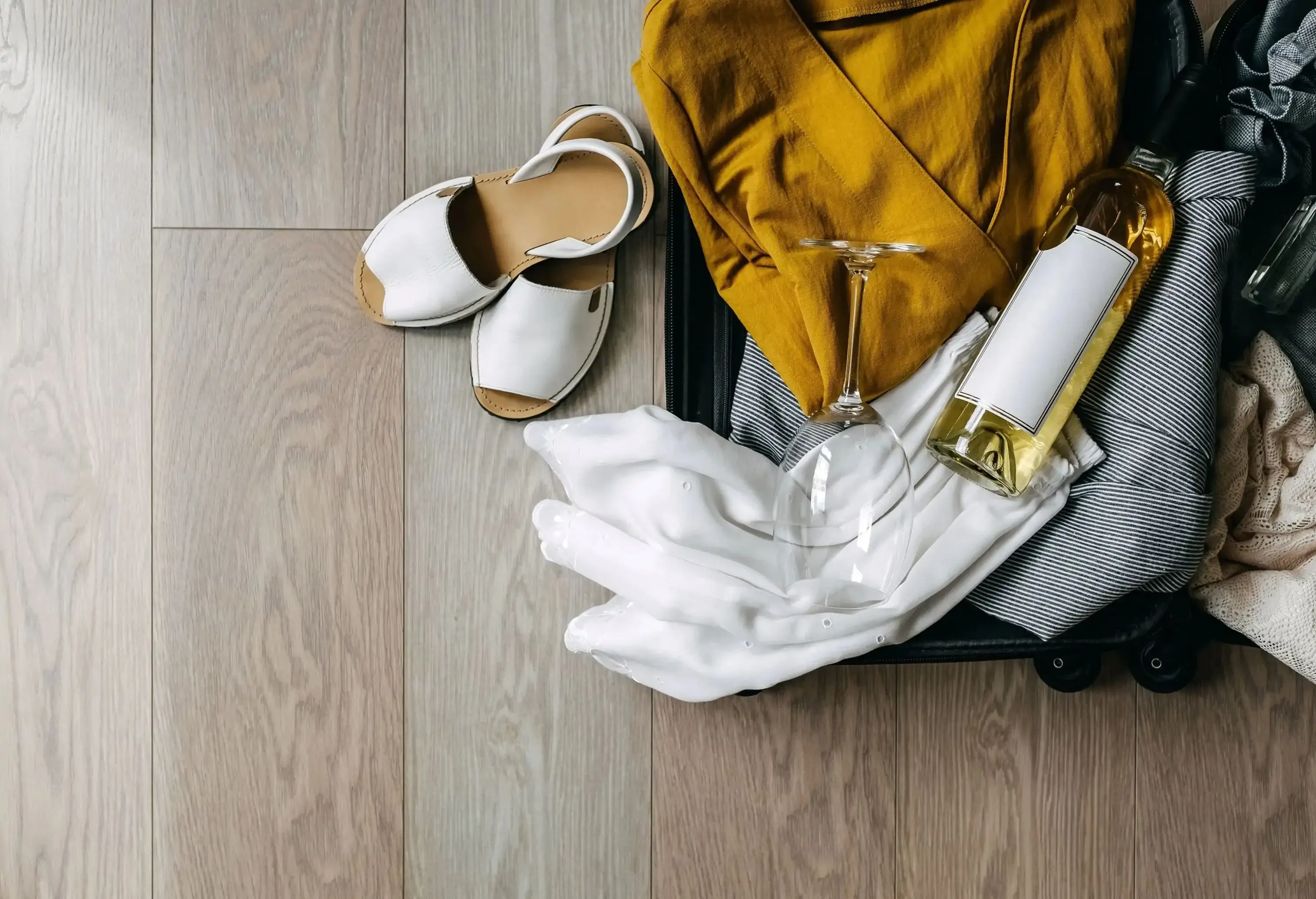 Open suitcase full of summer clothes, a camera and wine bottle, packing for travel.