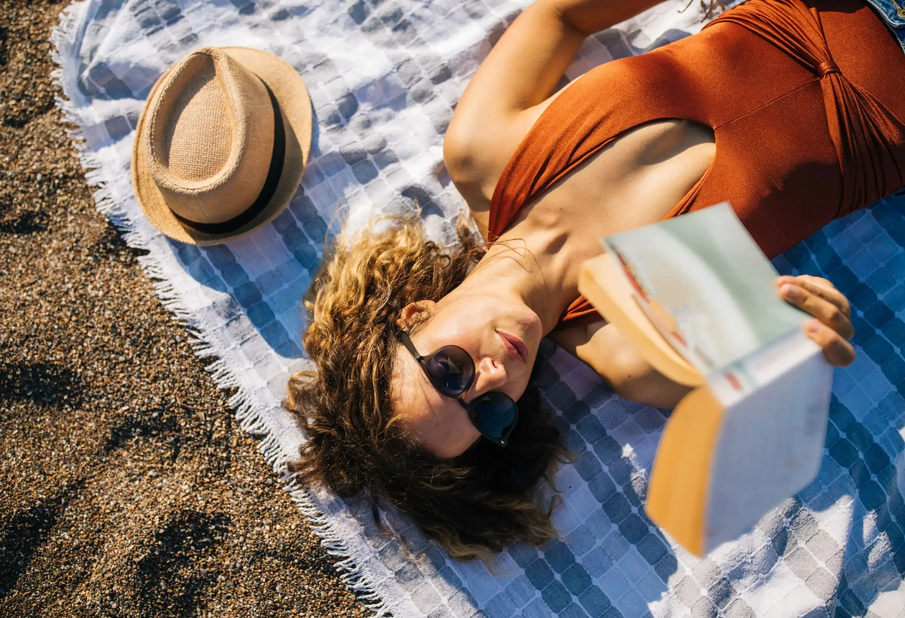 A woman lying on the beach in the sand and reading a book