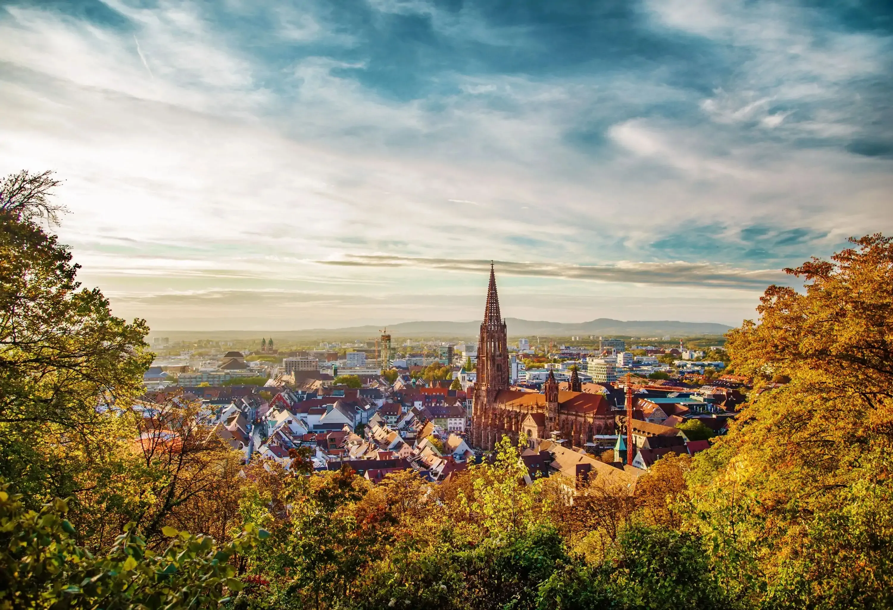 A medieval Gothic church with a towering spire dominates the city's skyline against the cloudy blue sky.