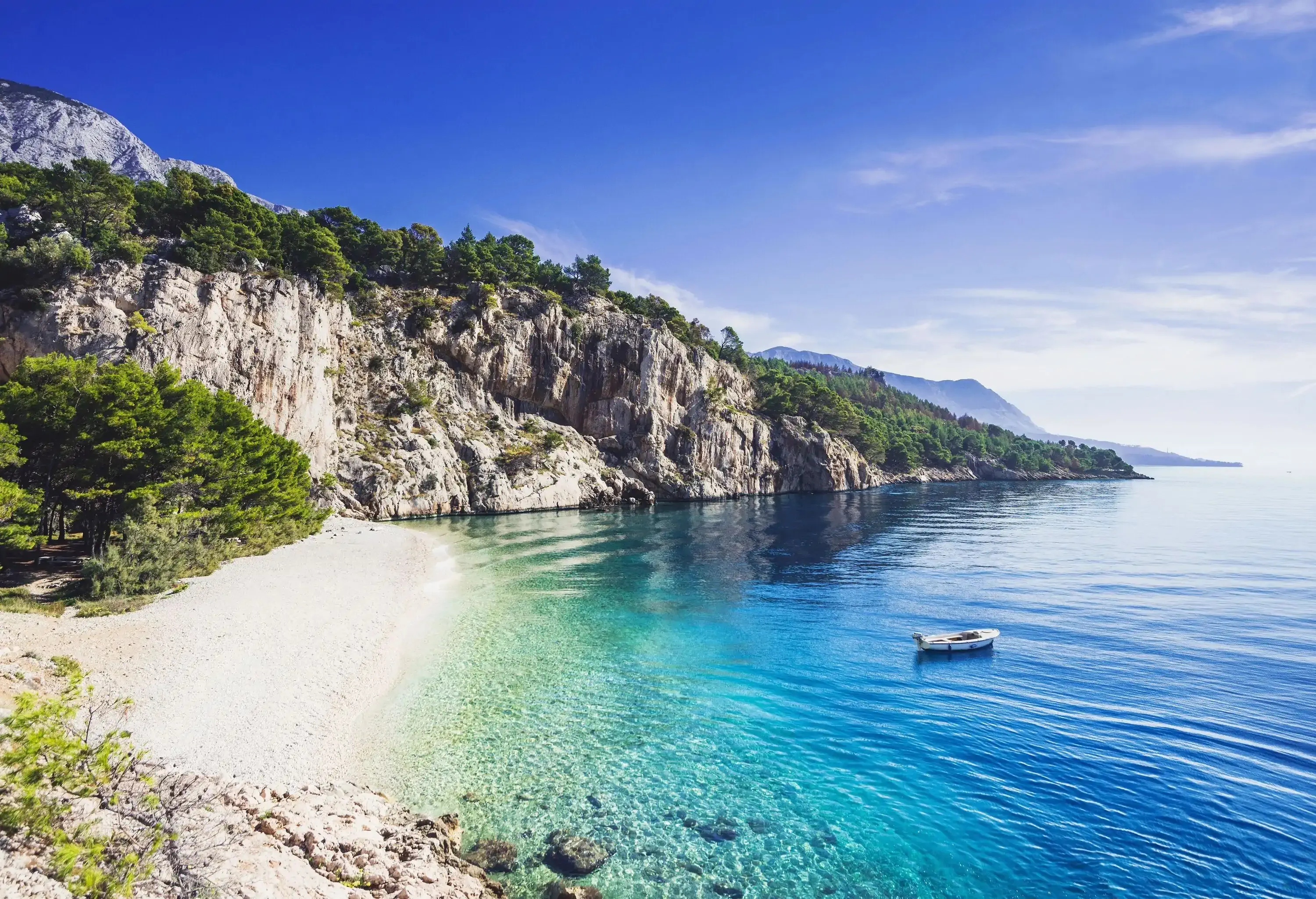 A picturesque pebble beach with a small boat moored on the crystalline tranquil turquoise water surrounded by cliffs.