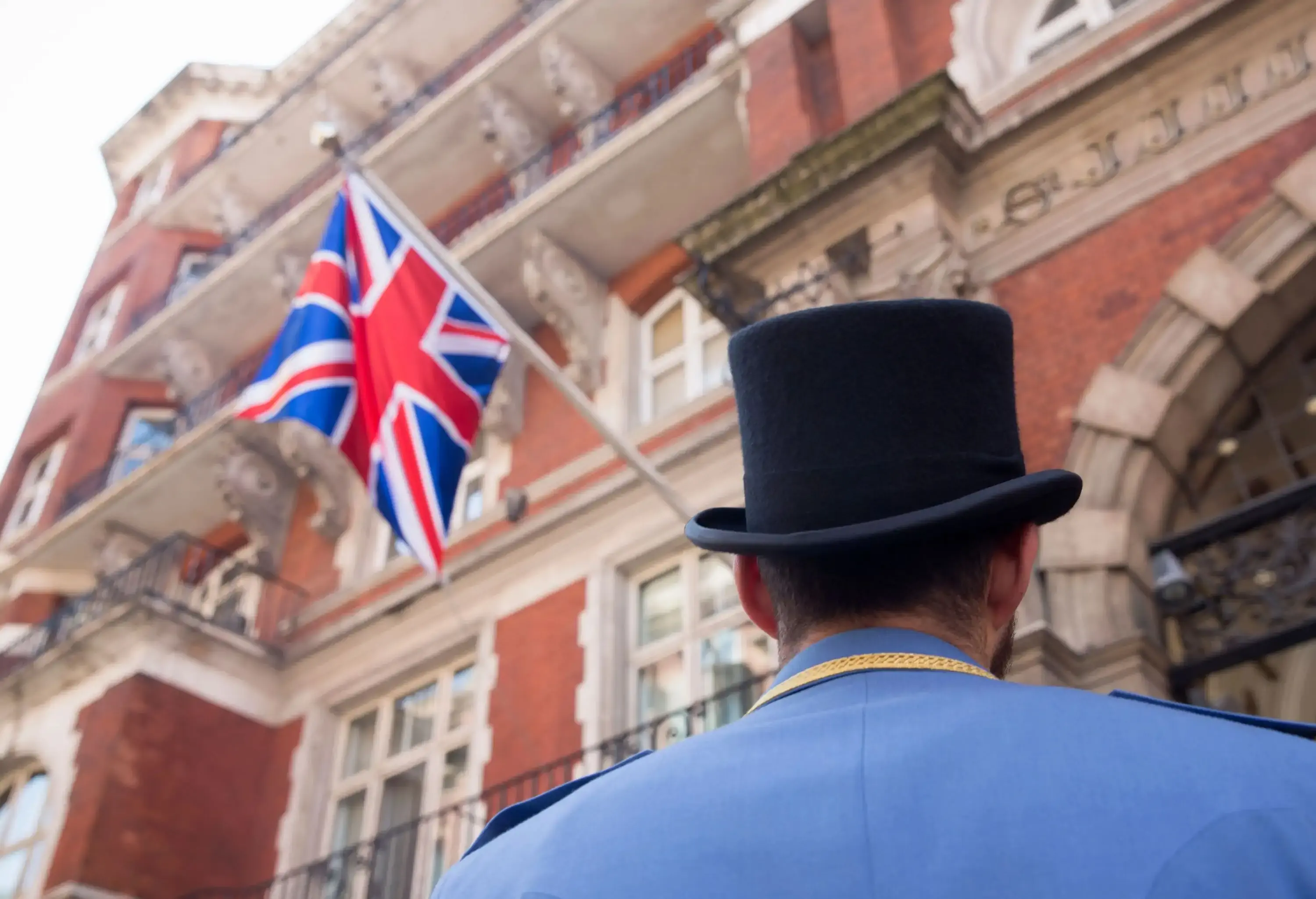 Back view of a doorman standing in front of a building with a British flag hung on the balcony.
