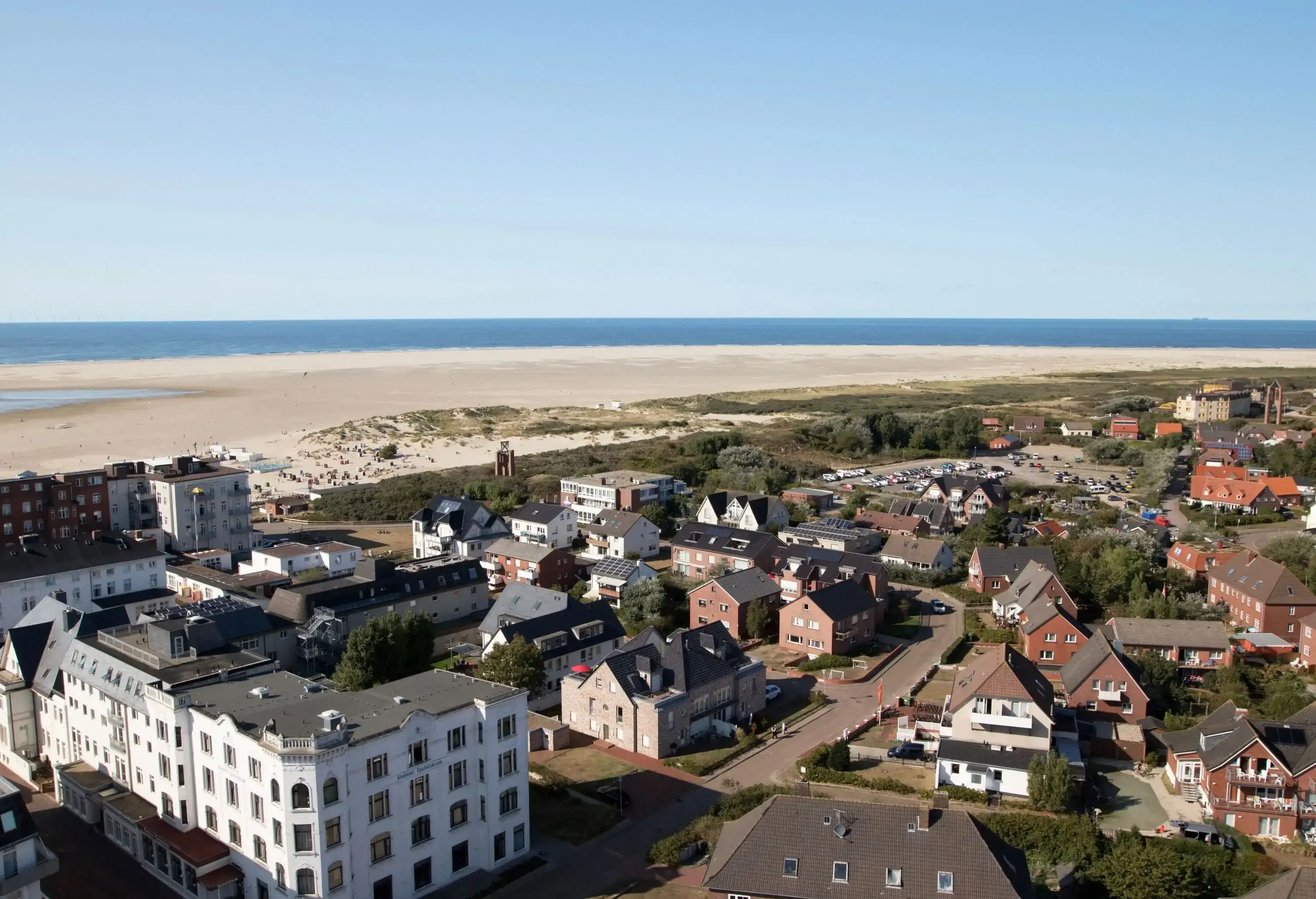 A town on the coast across from a broad beach under a clear sky.