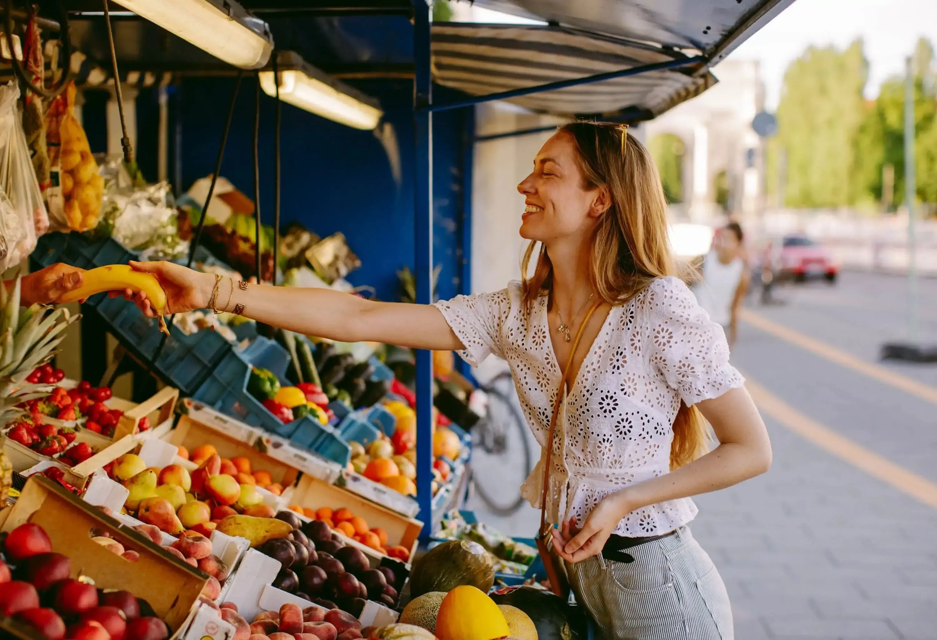 A woman buying a banana from a fruit stand with a variety of fruits on display.