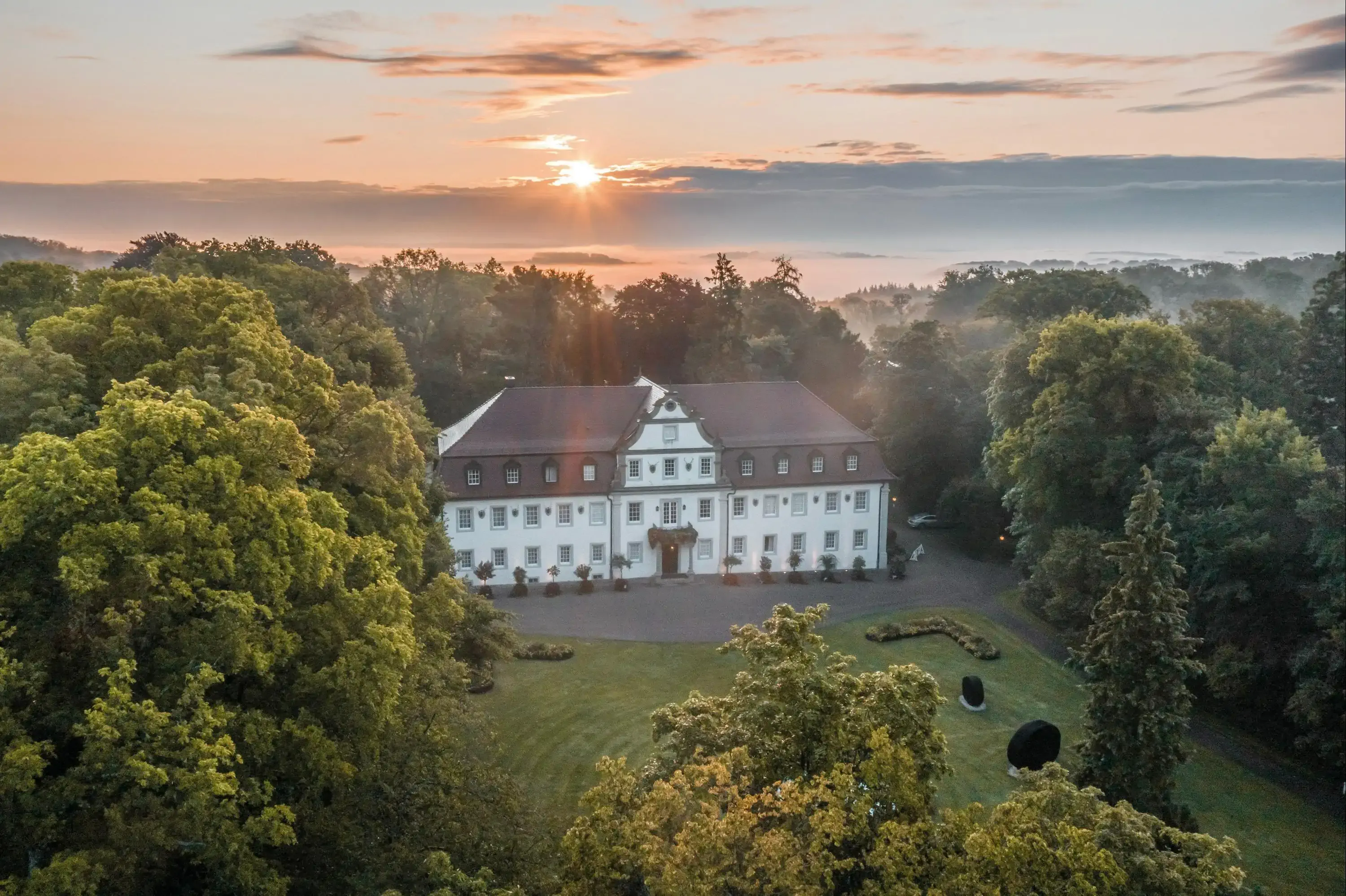 Aerial view of castle hotel in the middle of a forest at sunset