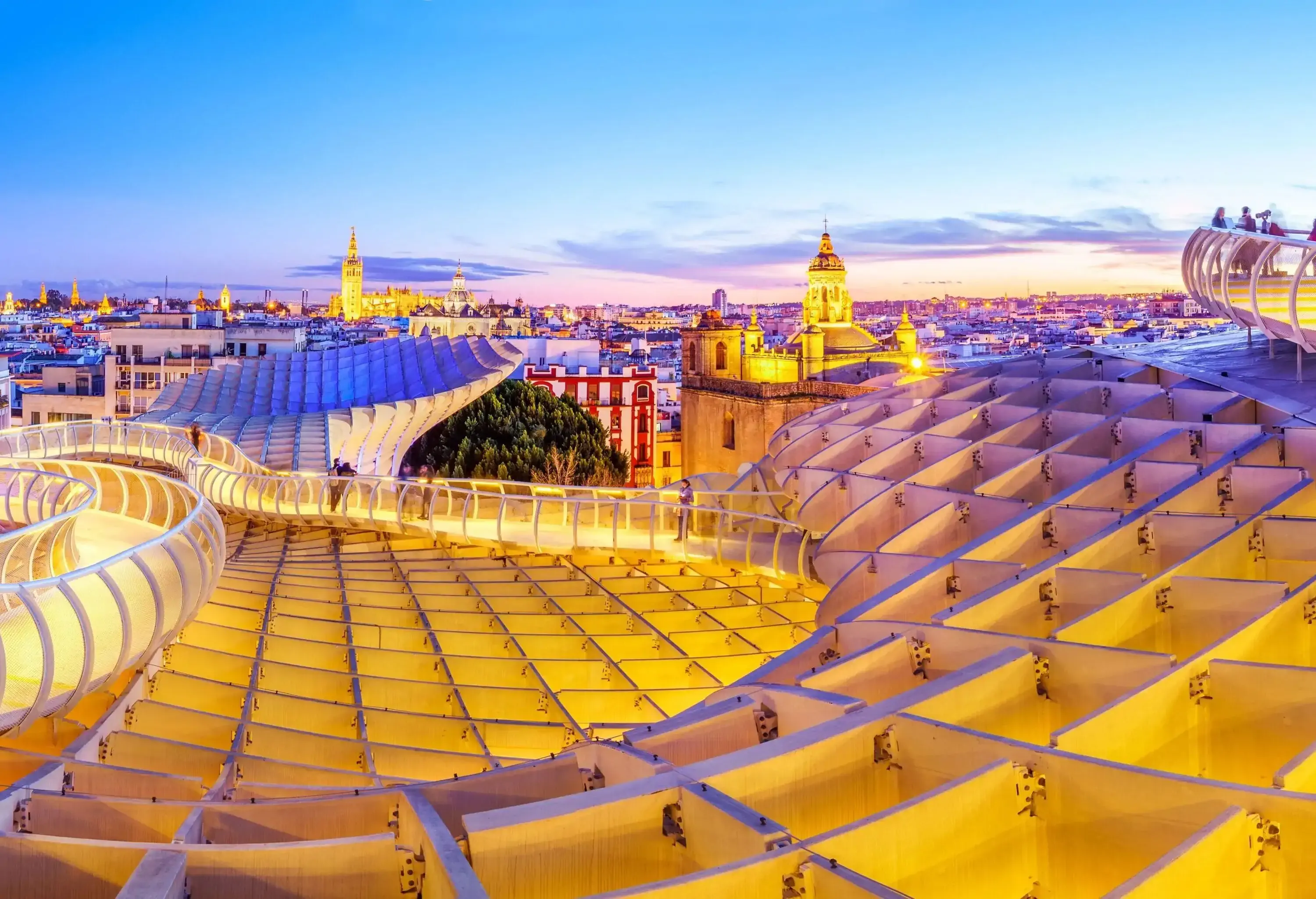 A winding balcony with cityscape views across an illuminated structure designed with patterns of intersecting lines.