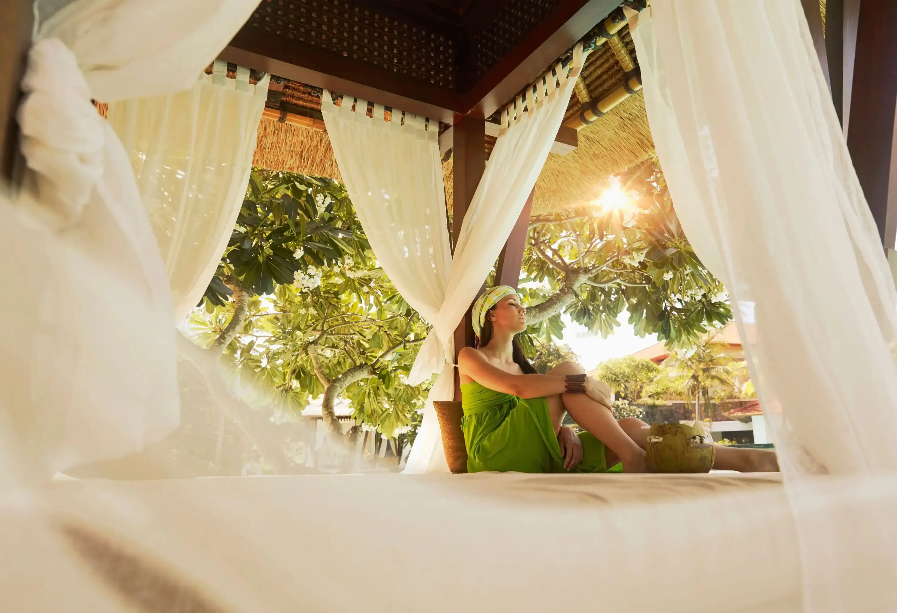 A woman sitting on a four poster bed with floaty muslin at a tropical resort