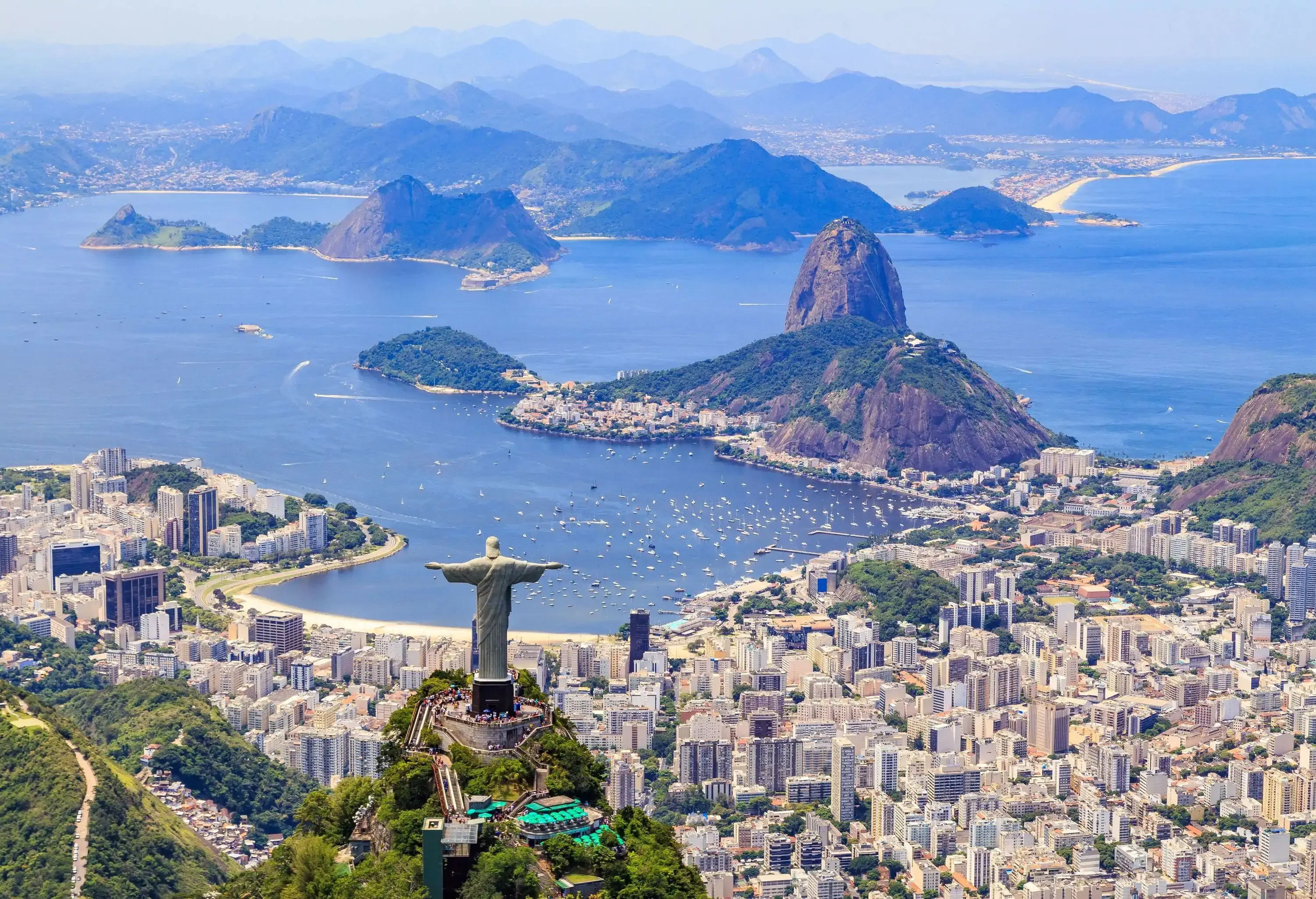 The iconic Christ the Redeemer monument and the majestic Corcovado Mountain overlook the coastal city below, along with the picturesque Sugarloaf Mountain and the tranquil Botafogo Bay.