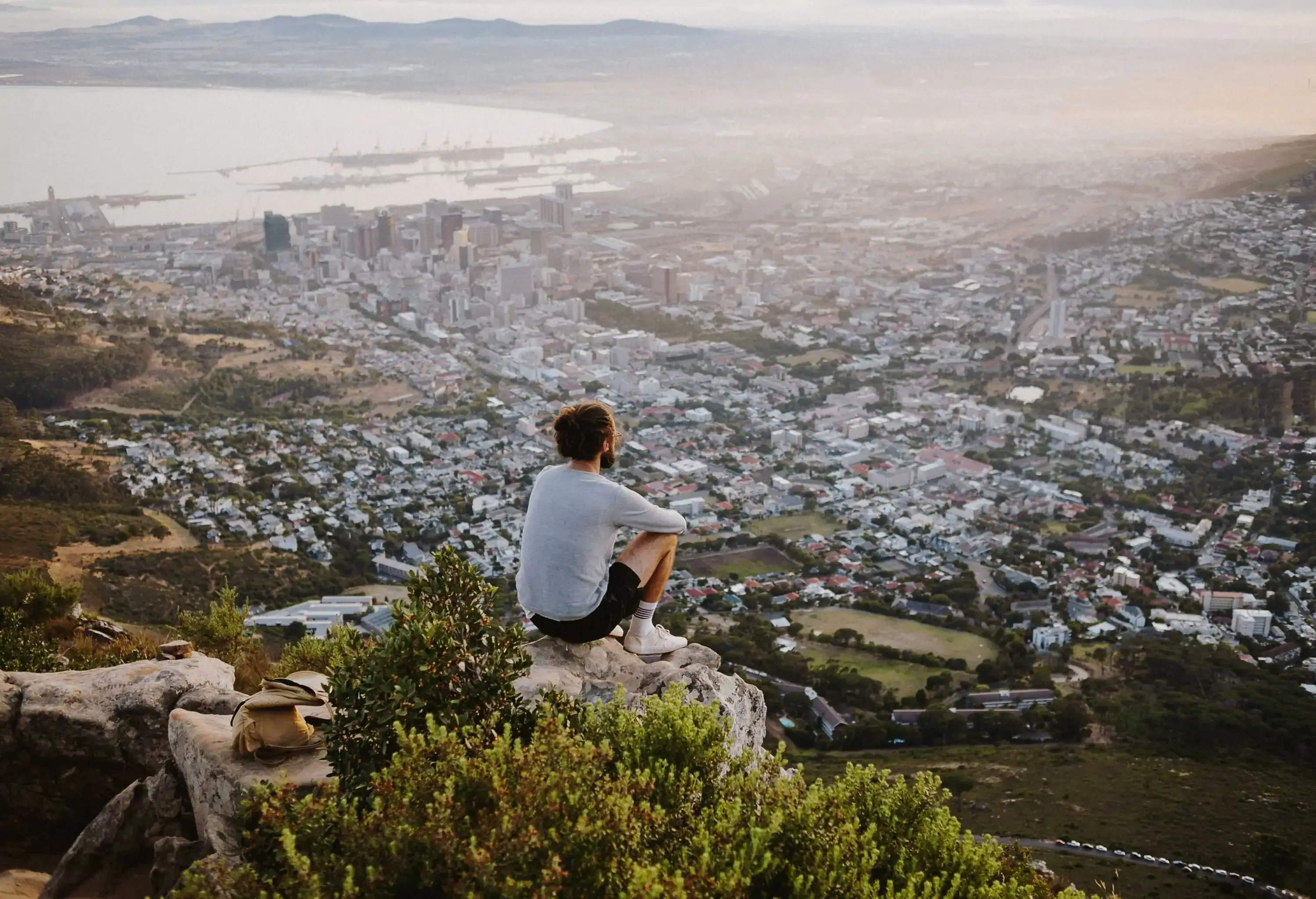 A man sits on the summit overlooking the vast and hazy coastal town.