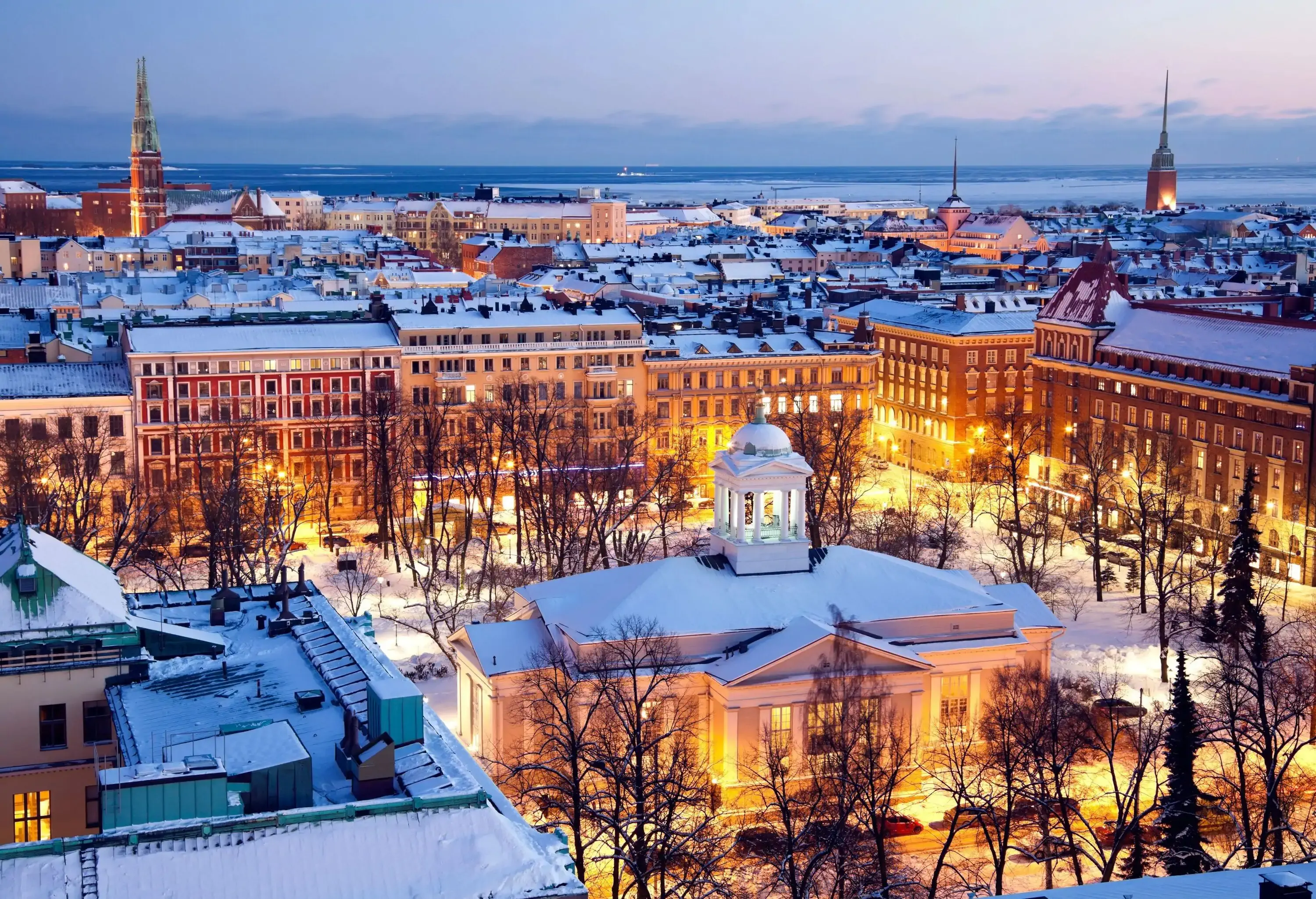 Helsinki, Finland skyline cityscape with snow-covered roofs and an illuminated church park in the centre.