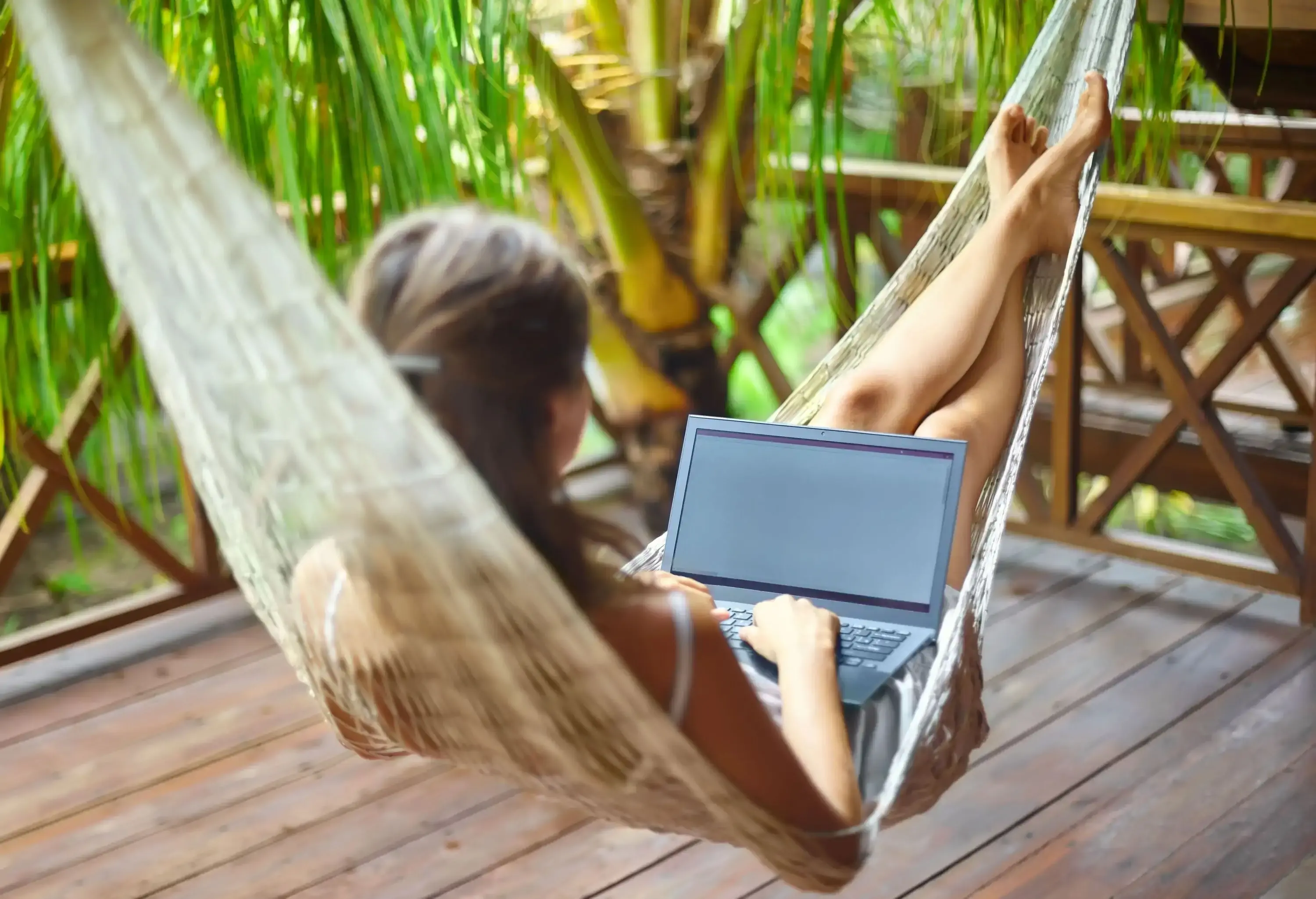 A woman in a hammock on a balcony, working on her laptop.