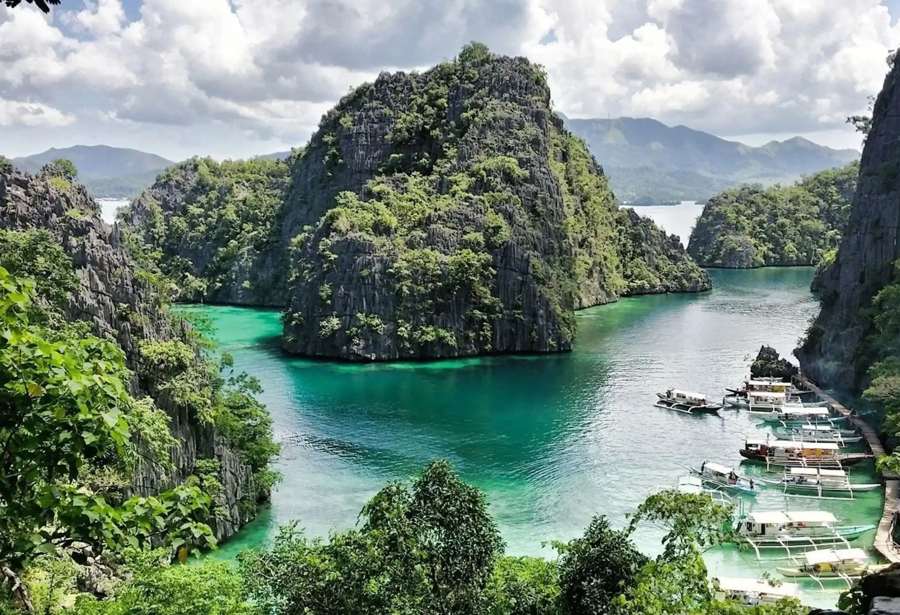 Tourist boats docked along the boardwalk along the stunning limestone rock formation emerging on the sea.
