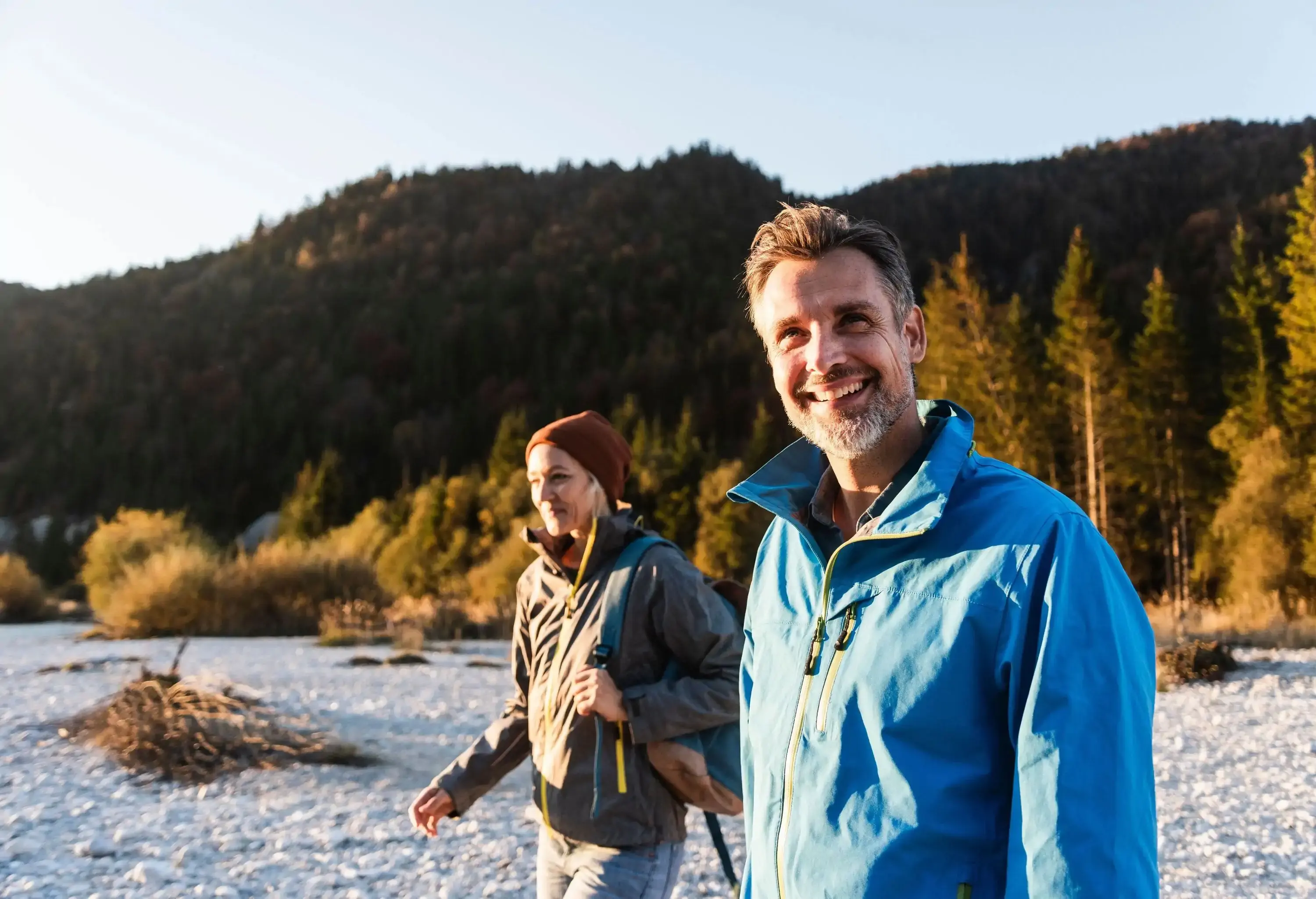 A happy couple hiking on a rocky path, against a backdrop of dark hills and trees.