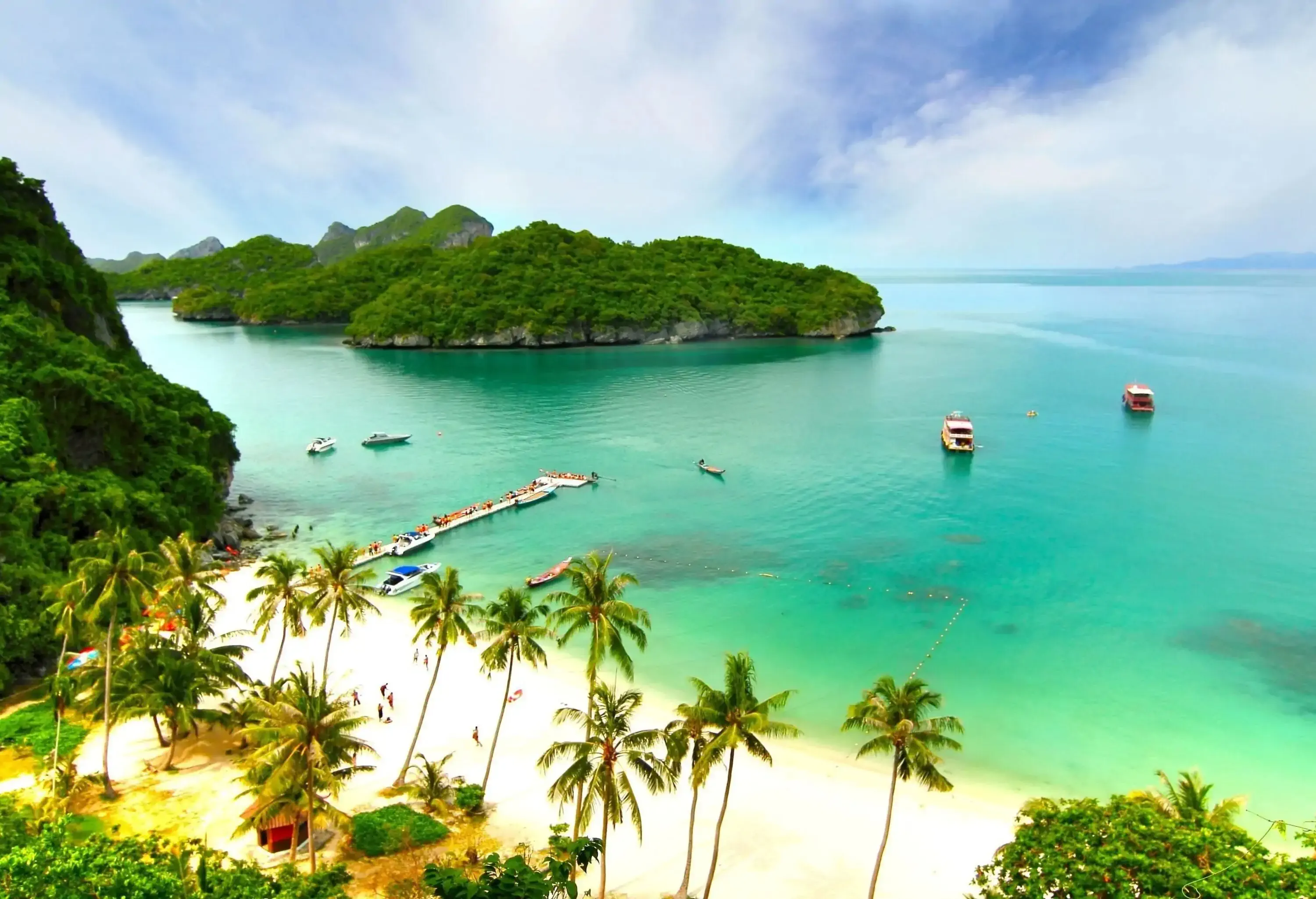 Boats anchored in the calm sea, which is dotted with wooded islands.