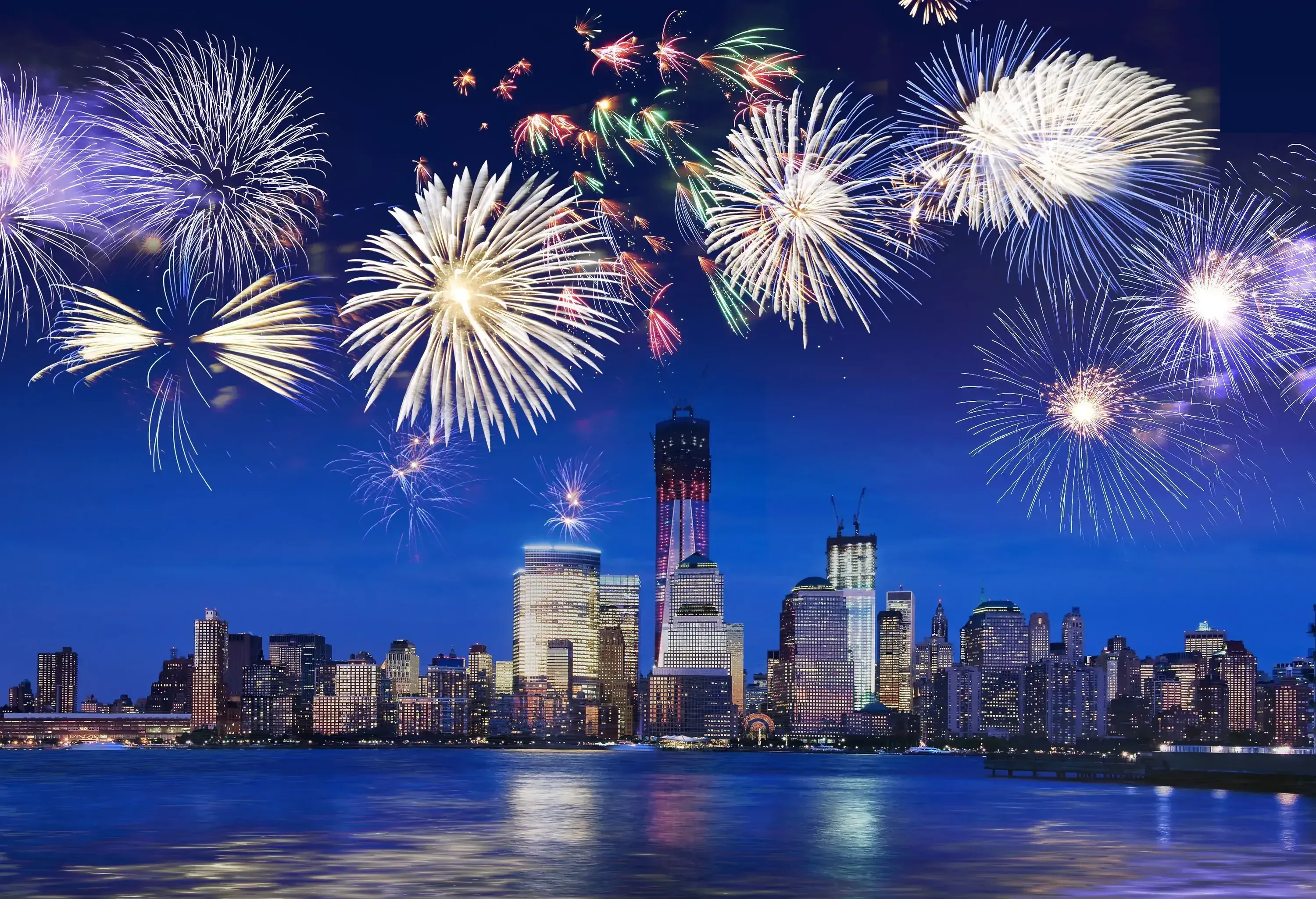 Colourful fireworks explode in the sky against the stunning city skyline on the waterfront. 