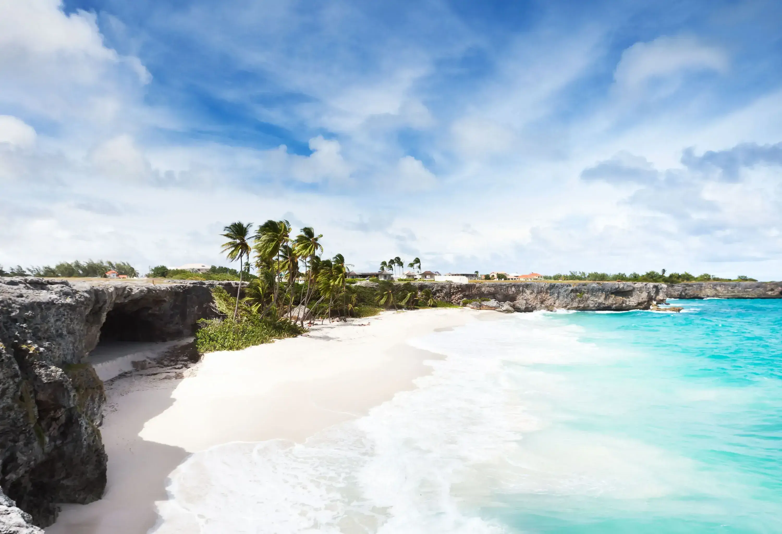 High coral cliffs line the turquoise beach with white waves rolling into the shore on a scenic sky.