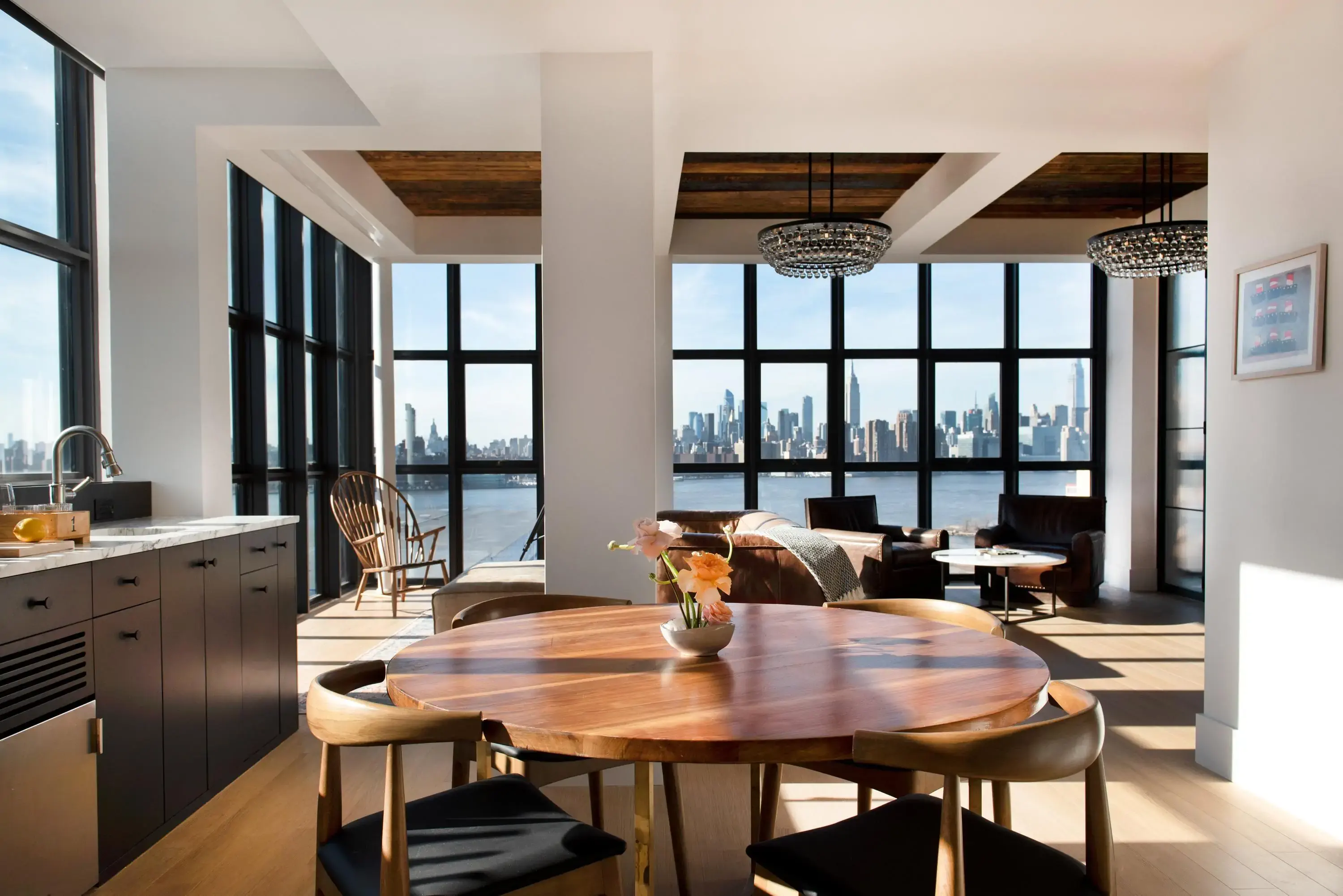 A minimalist aparthotel kitchen with a wooden table overlooking a river and city skyline