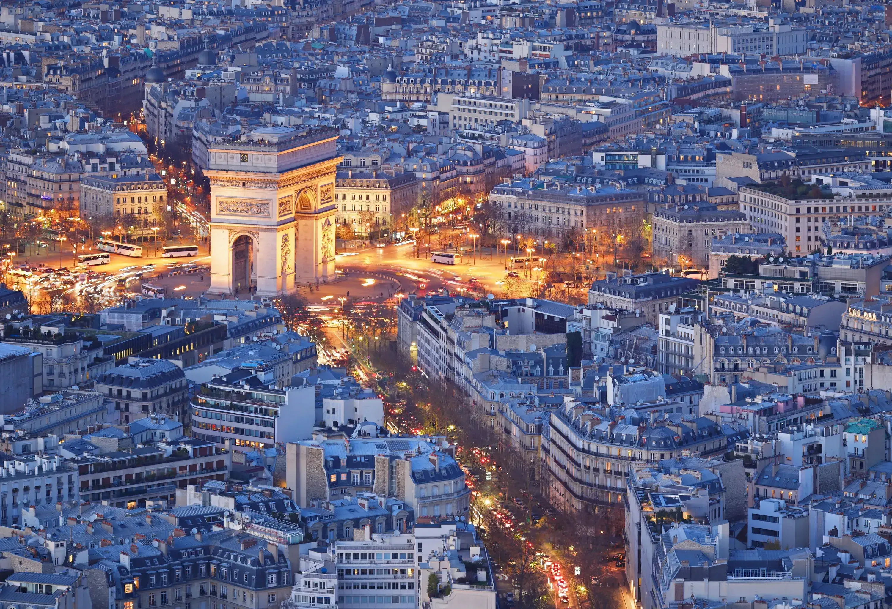 The Paris cityscape at night with the Arc de Triomphe surrounded by lit avenues.