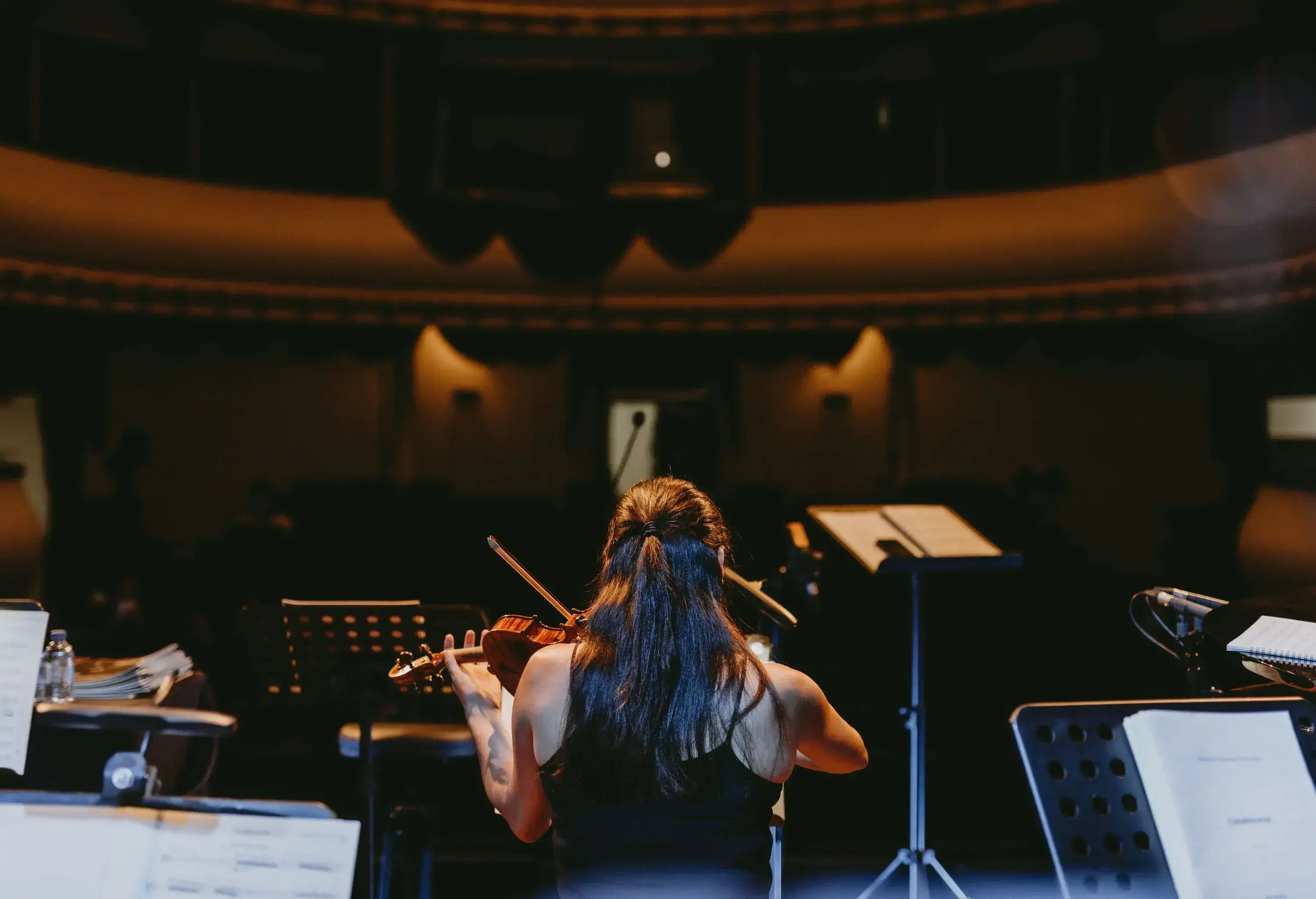 A musician sits while playing a violin on the stage.