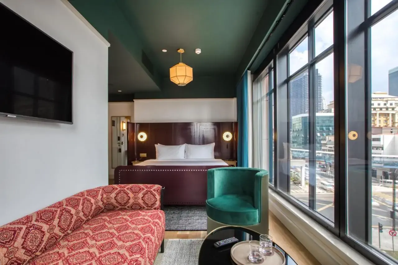 Modern Asian hotel room with sofa and a bed with large windows looking over cityscape