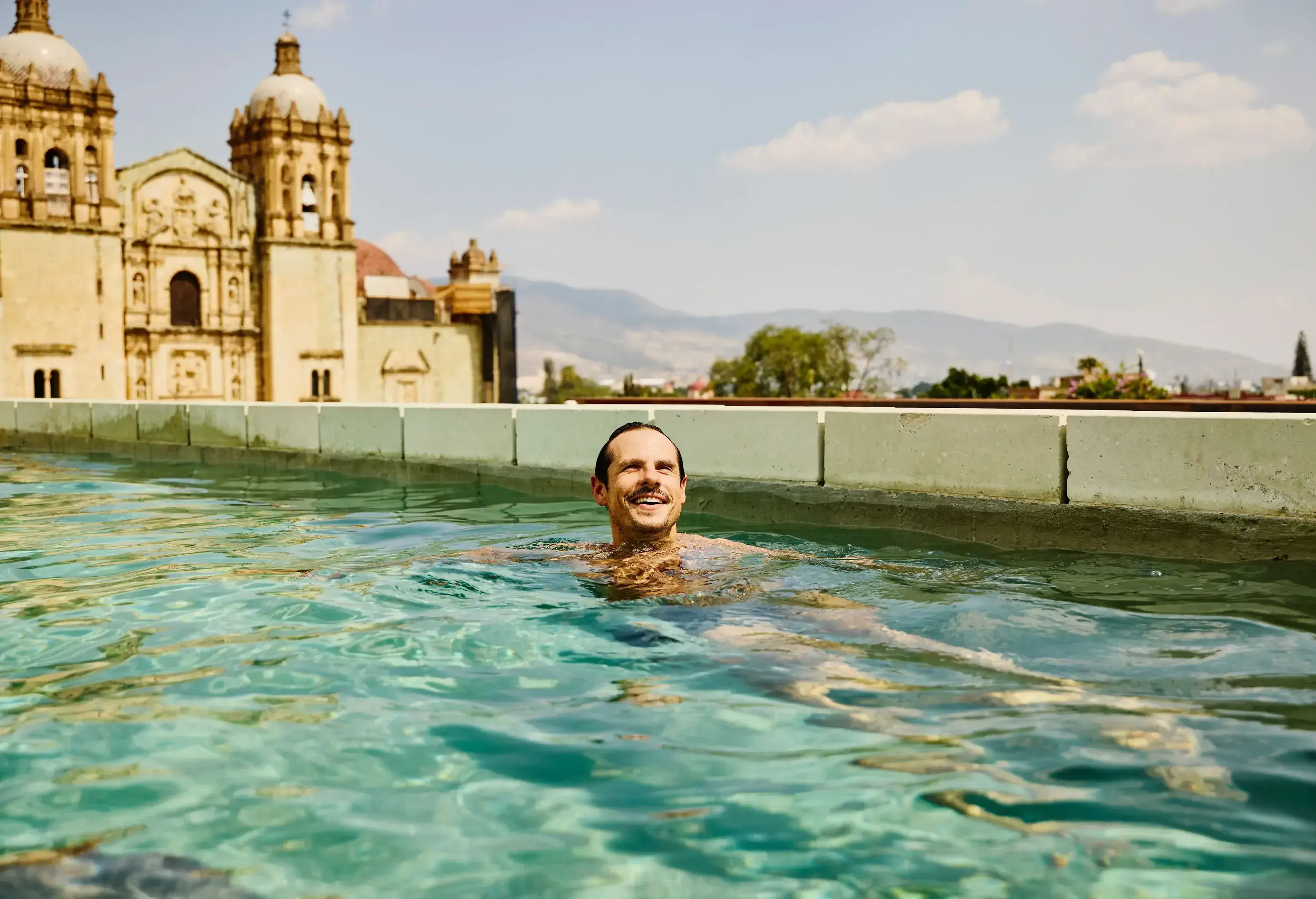Medium wide shot smiling man swimming in rooftop pool while on vacation in Oaxaca, Mexico