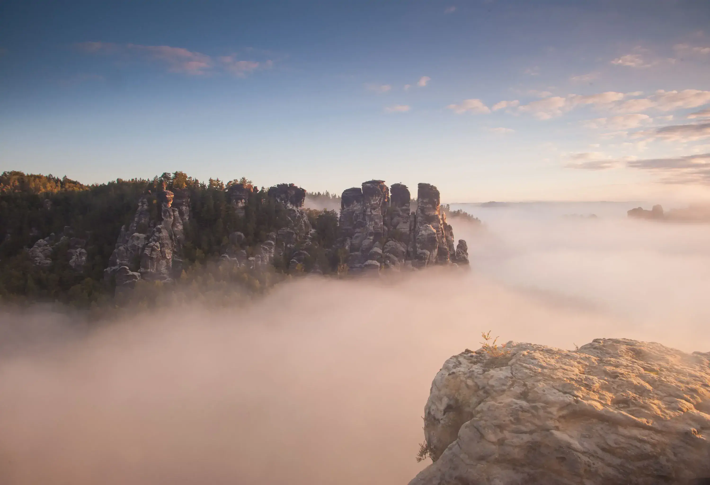 Towering rock formations surrounded by fog under the clear blue sky.