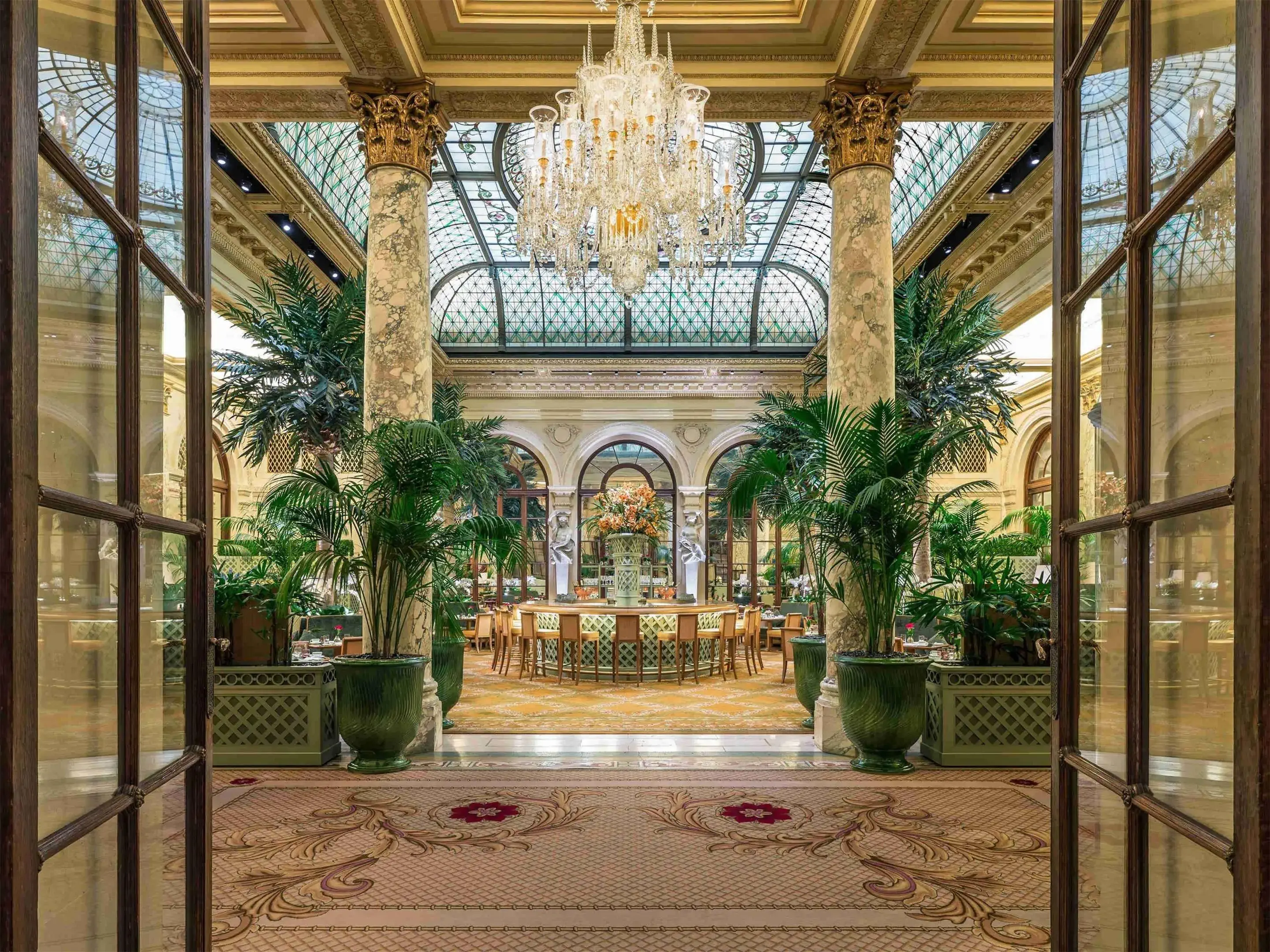 A luxurious hotel bar and restaurant with a glass roof, chandelier and exotic plants in art nouveau style