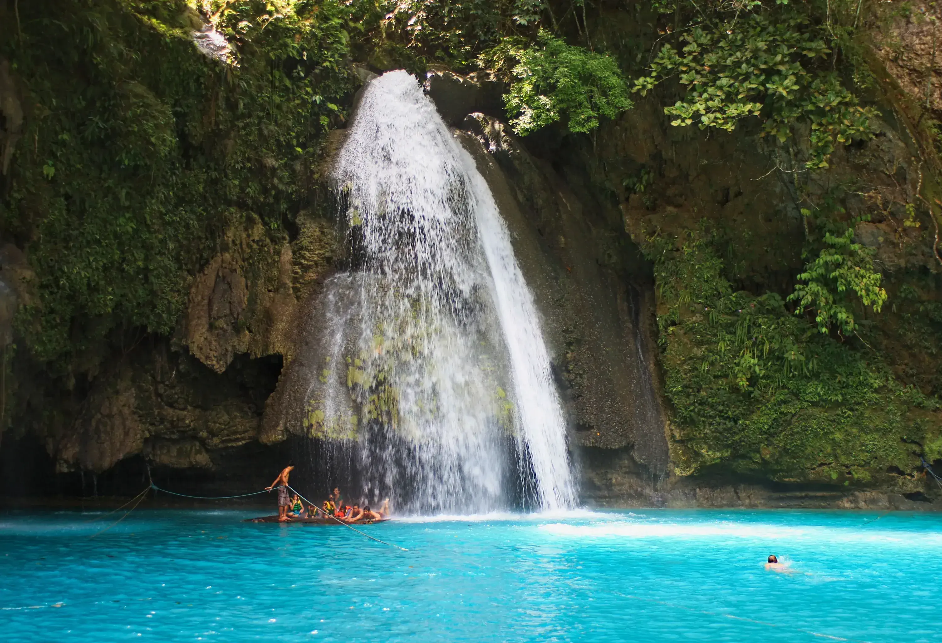 A waterfall cascades from a steep cliff into a stream with light blue waters.