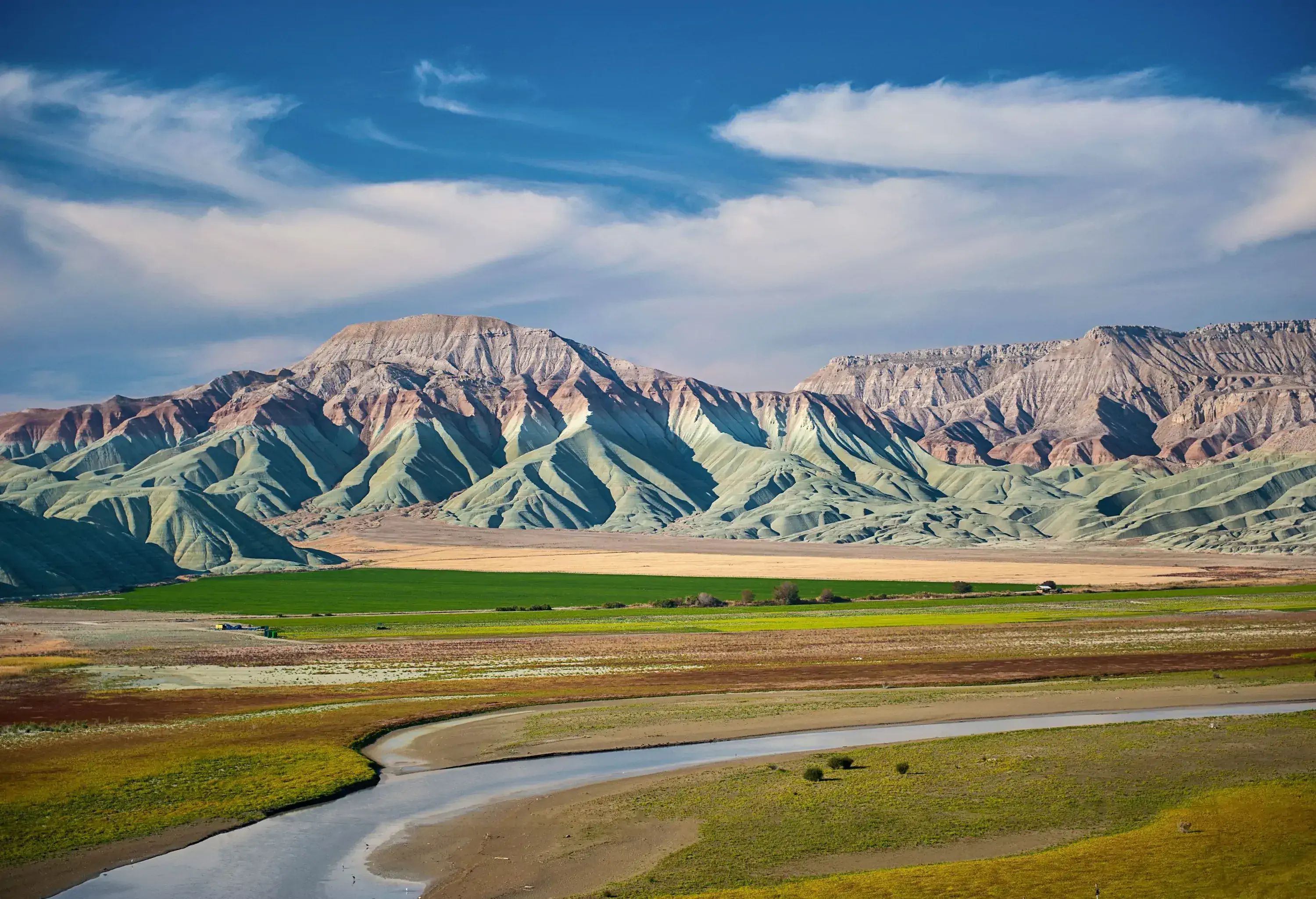 A bald mountain range envelops a lush and verdant land, with a peaceful stream flowing gently through the landscape.