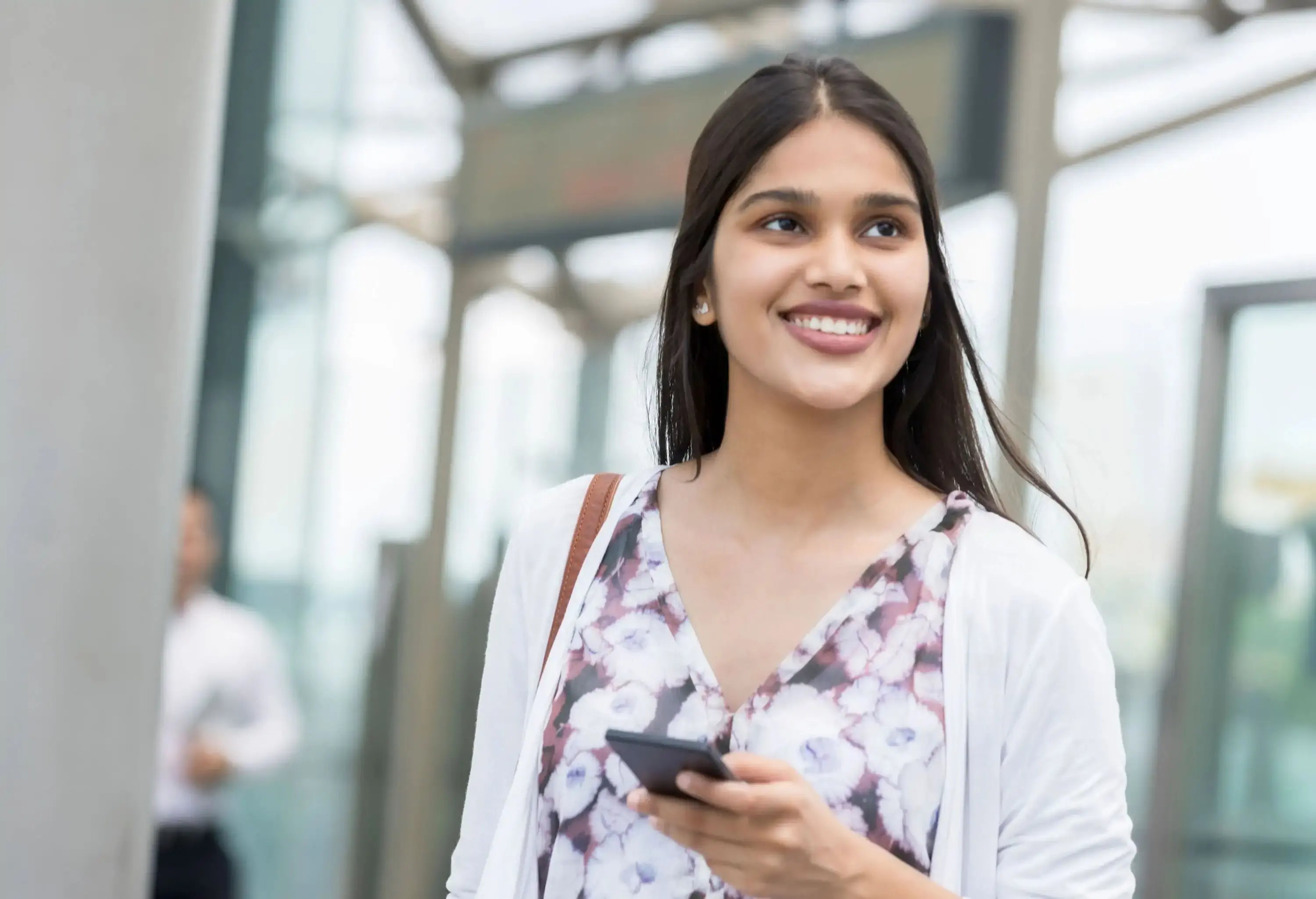 A long-haired woman holding a phone while looking into the distance with a smile.